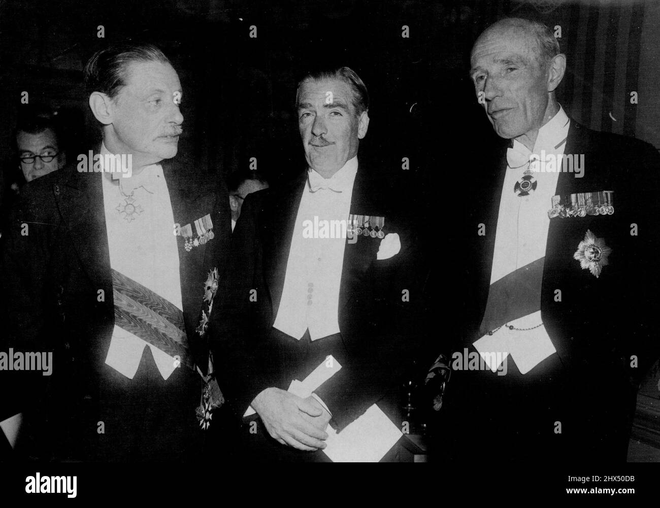 Herr Eden und die Pilger -- von links nach rechts der Vorsitzende der Pilger, Sir Campbell Stuart, Herr Eden und Lord Halifax, ein ehemaliger Außenminister. Mehr als 450 Gäste besuchten gestern Abend das Pilgeressen im Savoy Hotel, London. Der Außenminister, Herr Eden, hielt nach dem Abendessen die Rede des Hauptleiters. Er sprach 30 Minuten lang unter beständiger Applaus. Er gab das Thema seiner Rede, als er sagte: „Alle Dinge sind möglich, solange drei die Einheit und das gegenseitige Verständnis zwischen dem Britischen Commonwealth und den Vereinigten Staaten von Amerika sind. Konstruktive Erfolge sind nicht möglich, wenn wir Stockfoto