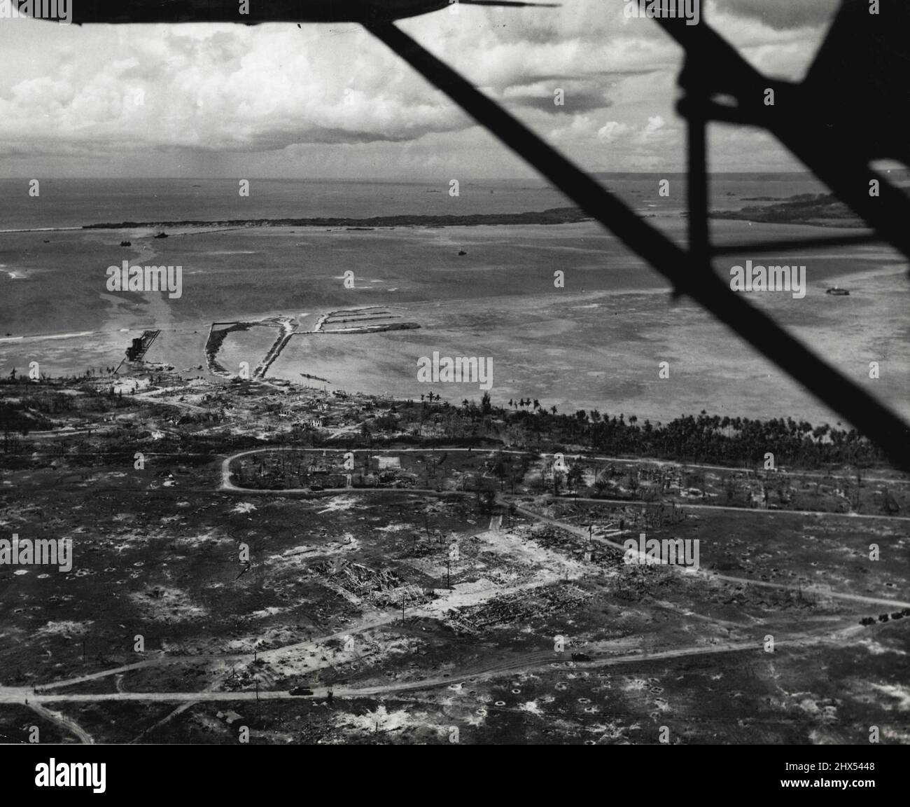Guam-Szene -- Dieses Luftbild zeigt die Ruinen der Marine Barracks (unten) und der Stadt Sumay auf der Orote Peninsula, Guam, die von den Marineinfanteristen nach einem grandiosen Flug- und Marineschlagen wieder erobert wurden. Im Hintergrund ist Carbes Island (links) und der Piti Navy Yard (rechts, zwischen den Tragflächen des Flugzeugs) zu sehen. 08. Juli 1944. (Foto vom offiziellen US Marine Corps-Foto). Stockfoto