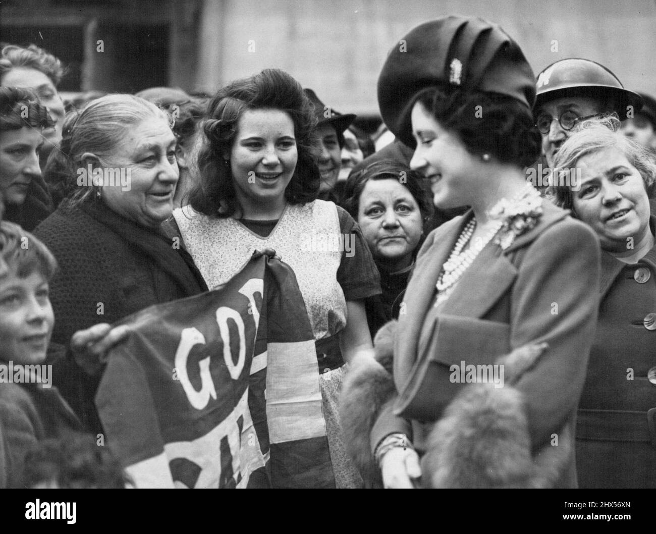 King und Queen Touren durch Gebiete, die durch Luftangriffe im East End von London beschädigt wurden. Ihre Majestät plaudert während der Tour mit einer Frau, die eine Flagge mit der Aufschrift „Gott rette den König“ hält. 16. Juni 1941. (Foto: Fotos der Londoner Nachrichtenagentur). Stockfoto