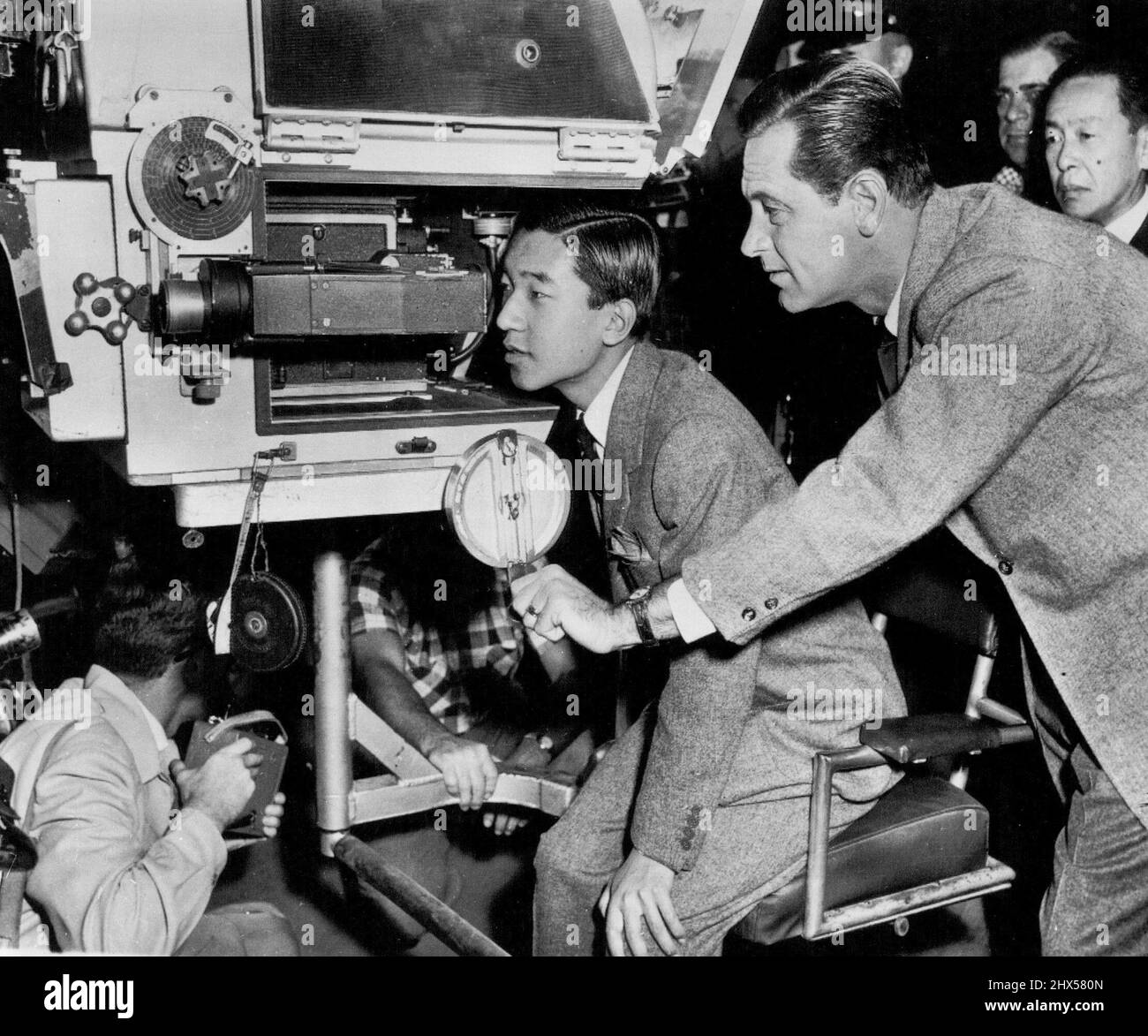 Japanese Prince Tours Movie Studio -- Kronprinz Akihito von Japan schaut heute während einer Tour durch die Metro-Goldwyn-Mayer-Filmstudios durch den Sucher einer Filmkamera. Der Schauspieler William Holden erklärt dem Prince, der unter der Schirmherrschaft des State Department viele Teile der Vereinigten Staaten besucht, die Bedienung der Kamera. 30. September 1953. (Foto von AP Wirephoto). Stockfoto