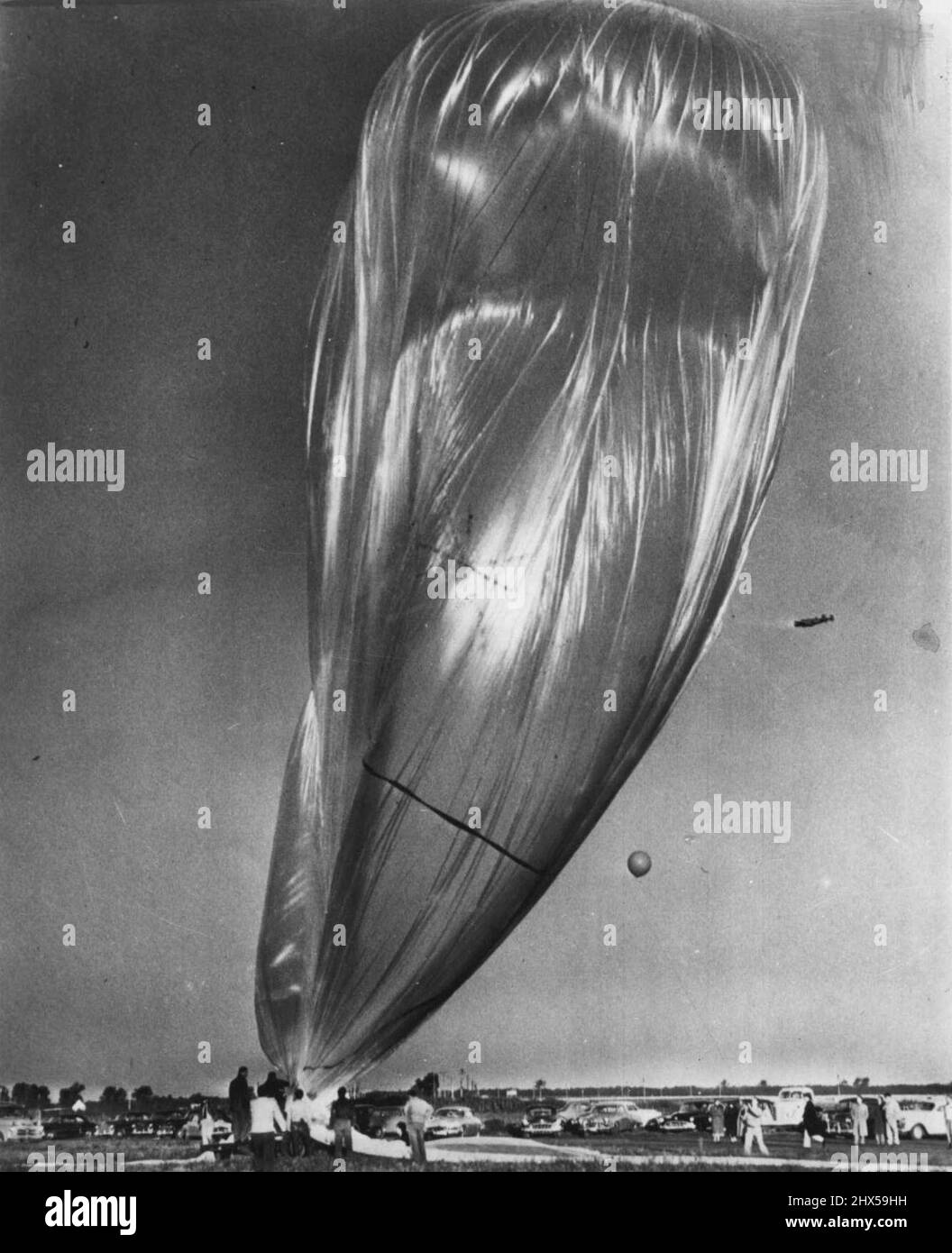 'Giant Skyhook' startbereit -- der größte bekannte unbemannte Ballon steht vor seinem Anker und soll heute früh starten. Der Ballon sollte Instrumente mit kosmischer Strahlung tragen, die etwa 23 Meilen hoch waren, aber Löcher entwickelten sich in dem zerbrechlichen Kunststoff und die Instrumentenlast wurde abgenommen. Es wurde beschlossen, die Ballons trotzdem zu veröffentlichen, um Erfahrungen zu sammeln. Der Big wurde für das Büro der Naval Research gebaut, um kosmische Strahlung besser zu untersuchen. Abgebildet sind die oberen 100 Fuß des Ballons, der 287 Fuß lang war. Der kleine auf der rechten Seite ist ein Luftballon, der den Wind erkennt. 03. September 1952. (Foto von Stockfoto