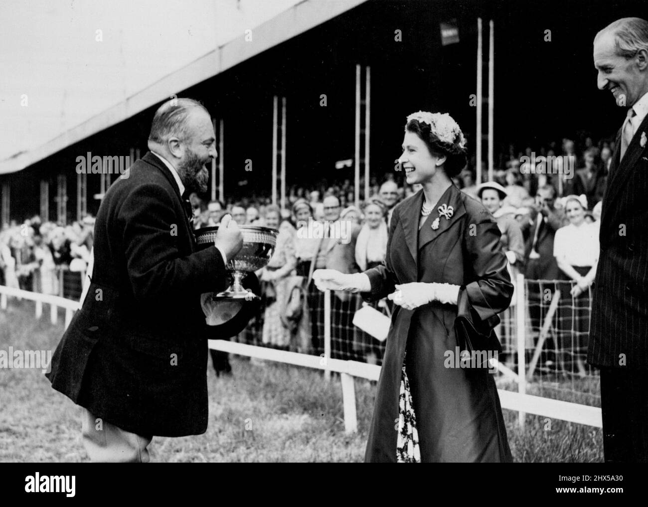 Königliche Besucher bei der Royal Show -- H.M., die Königin, hat gestern bei ihrem Besuch bei der Royal Show in Nottingham den Silver Challenge Cup dem Sieger der Hunter Class, Major Michael Beaumont aus Brannockstown, Co. Kildare, vorgestellt. Ihre Majestät trägt einen passenden Preis in königsblauer Seide, über einem Blumenkleid, mit einem winzigen, von Hand umarmenden Hut aus rosa Blumen. H.M. the Queen und H.R.H. der Herzog von Edinburgh besuchten am Mittwoch, dem 6.. Juli, dem zweiten Tag der Show, die Royal Agricultural Show 1955, die derzeit im Wollaton Park, Nottingham stattfindet. 7. Juli 1955. (Foto von Fox Photos). Stockfoto