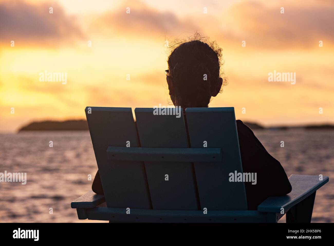 Die junge Frau sitzt am Strand und genießt den Sonnenuntergang über dem Meer Stockfoto