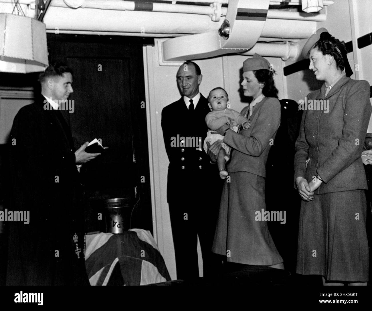 Eine ungewöhnliche Zeremonie wurde auf H.M.A.S. durchgeführt „Nepal“ in einem australischen Hafen, als vor kurzem die Schiffsglocke als Taufbecken für James Plunkett-Cole, Sohn von LT. Comdr. Und Mrs. John Plunkett-Cole, in der Kapitänskabine stattfand. Von links: R.A.N. Padre, Lt. Comdr. J. Plunkett-Cole, R.A.N. Frau J. Plunkett-Cole mit Kind und Frau Adair Middleton, Godmother. 29. September 1944. (Foto vom Commonwealth Department of Information). Stockfoto