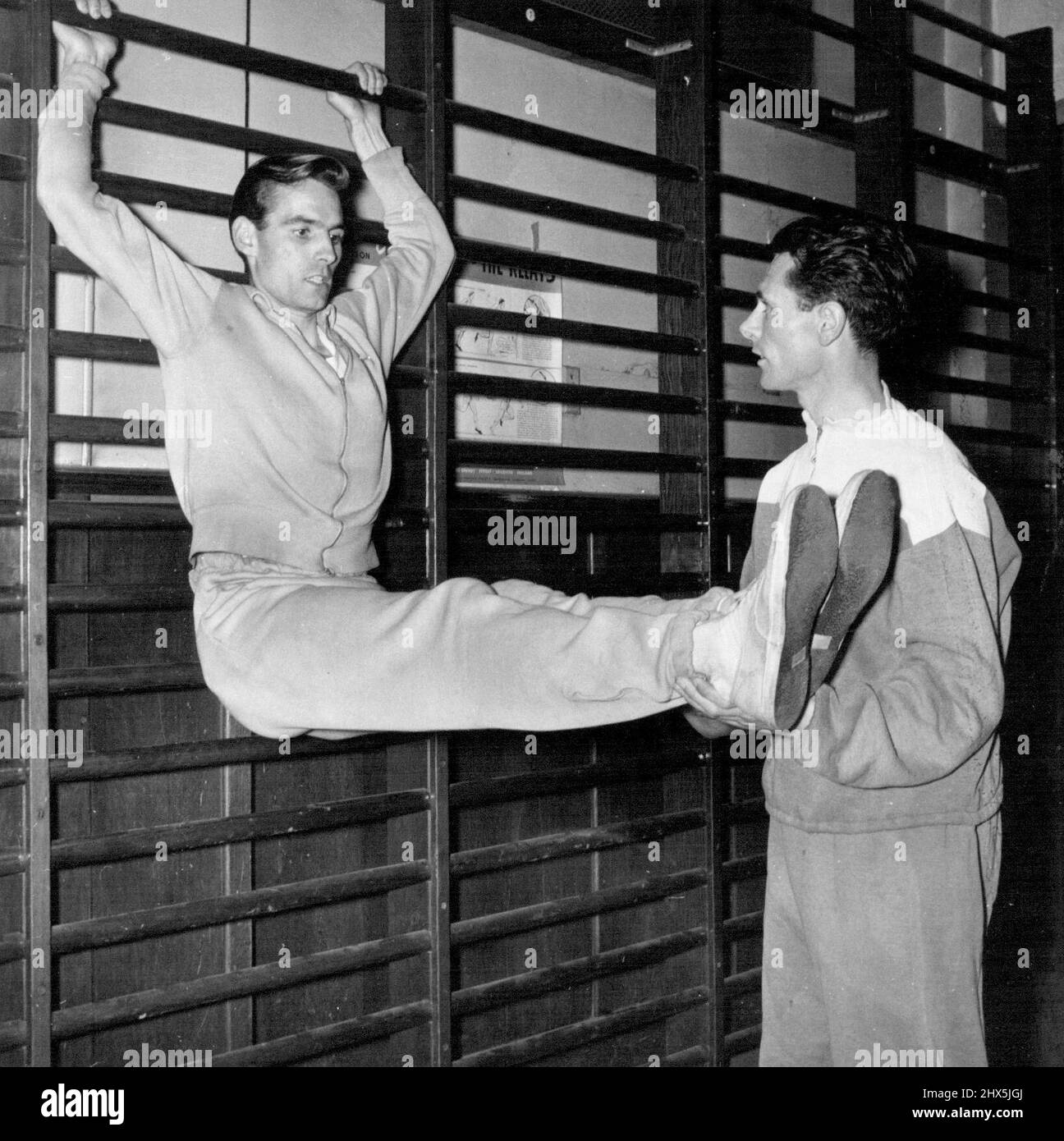 Wintertraining für Shirley der Überraschungs-Steeplechaser - Bill Coyne der A.A. Hon. Senior Coach, sah Eric Shirley von Finchley Harriers und Polytechnic Harriers durch eine Reihe von Übungen an den Wandstangen im Polytechnic Gyamasium, Regent Street, als Teil seiner Ausbildung in Vorbereitung auf die Olympischen Spiele im nächsten Jahr. Der Hindernisläufer Eric Shirley glaubte an ein ganzjähriges Training sowohl in der Turnhalle als auch auf der Rennstrecke, eine Politik, die sich sicherlich auszahlt. 26. Oktober 1955. (Foto von Fox Photos). Stockfoto