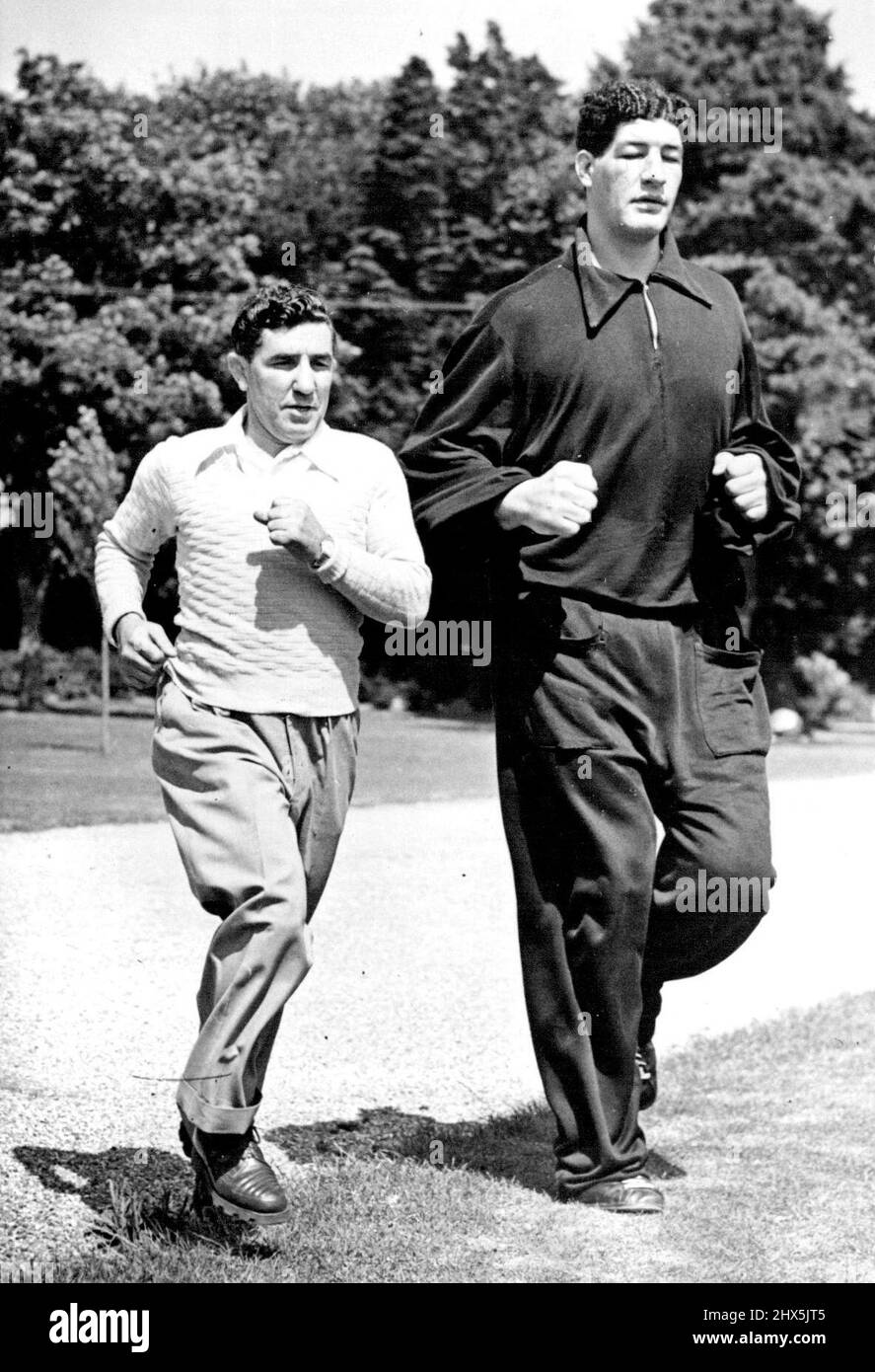 Der südafrikanische Boxer Ewart Potgieter überragt bei einem Trainingslauf in Brighton, England, seinen Trainer John holt. Potgieter ist 7ft 2in hoch und wiegt 22½st. 27. August 1955. Stockfoto