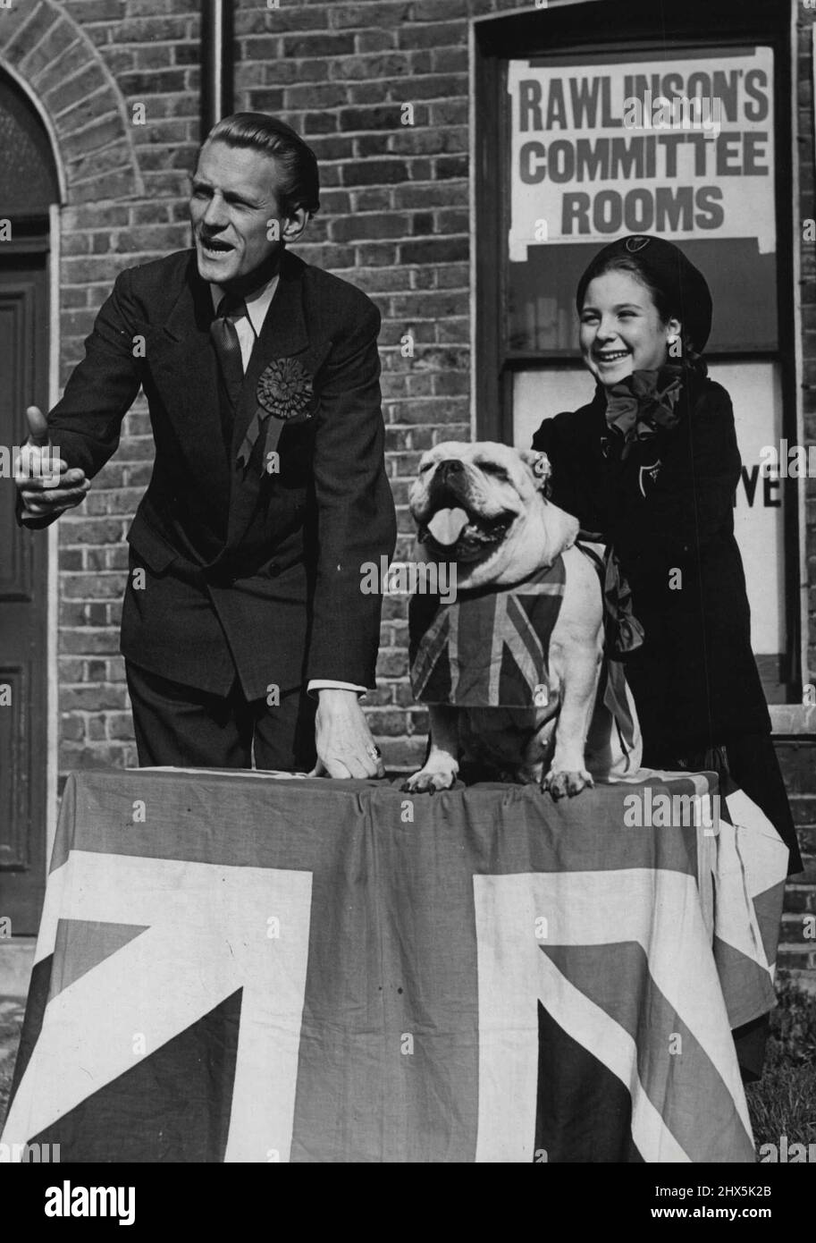 Churchill, der Bulldog, leitet das Meeting D/Van -- Herr Peter Rawlinson spricht vor einem Treffen im Freien vor seinen Ausschussräumen in Hackney. Chairman-like an seiner Seite ist 'Churchill', die Bulldogge mit seiner Geliebten, der 10-jährigen Mary Hickey. In seinem Wahlkampf hat Peter Rawlinson, Tory-Kandidat für Haokney, einen starken Unterstützer in Form einer Bulldogge namens 'Churchill', die ihm als Maskottchen geliehen wurde, die an vielen seiner Treffen teilnimmt und ihn auf Canvasing-Expeditionen begleitet. 23. Oktober 1951. (Foto von Fox Photos). Stockfoto