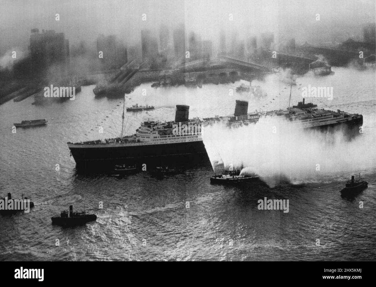 Die Königin Vervollständigt Die Junginnenreise Als Luxus-Liner -- Begleitet von Wasserströmung, die Feuerboote, Schlepper und andere Schiffe sowie Flugzeuge über den Kopf wirft, macht sich die britische Luxuslinerin Queen Elizabeth, das größte Schiff im Wasser, heute am frühen Morgen auf den Weg zum New Yorker Hafen, wo sie ihre erste Transatlantikreise im Passagierdienst absolviert. Die Königin machte viele Ozeanreisen mit Truppen während des Krieges, aber dies war ihre Jungfernfahrt, da sie als Luxusliner umgebaut wurde, das sie ursprünglich sein sollte. 21. Oktober 1946. (Foto von AP Wirephoto). Stockfoto
