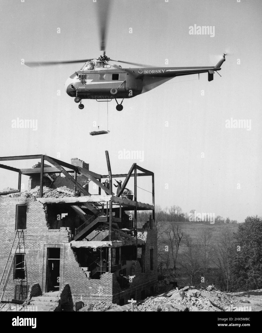 Ein „Bombenanfall“ auf einen Abfall wird im Rahmen einer Demonstration im National Civil Defense Training Center, Olney, MD, per Hubschrauber evakuiert. Das Zentrum wird von der Federal Civil Defense Administration durchgeführt. Es umfasst einen Stadtblock aus technischen Ruinen, die „ausgebombte“ Wohn- und Arbeitsstrukturen simulieren, um dem Aufseher und dem Rettungstraining größtmöglichen Realismus zu verleihen. 21. Januar 1955. (Foto von FCDA). Stockfoto