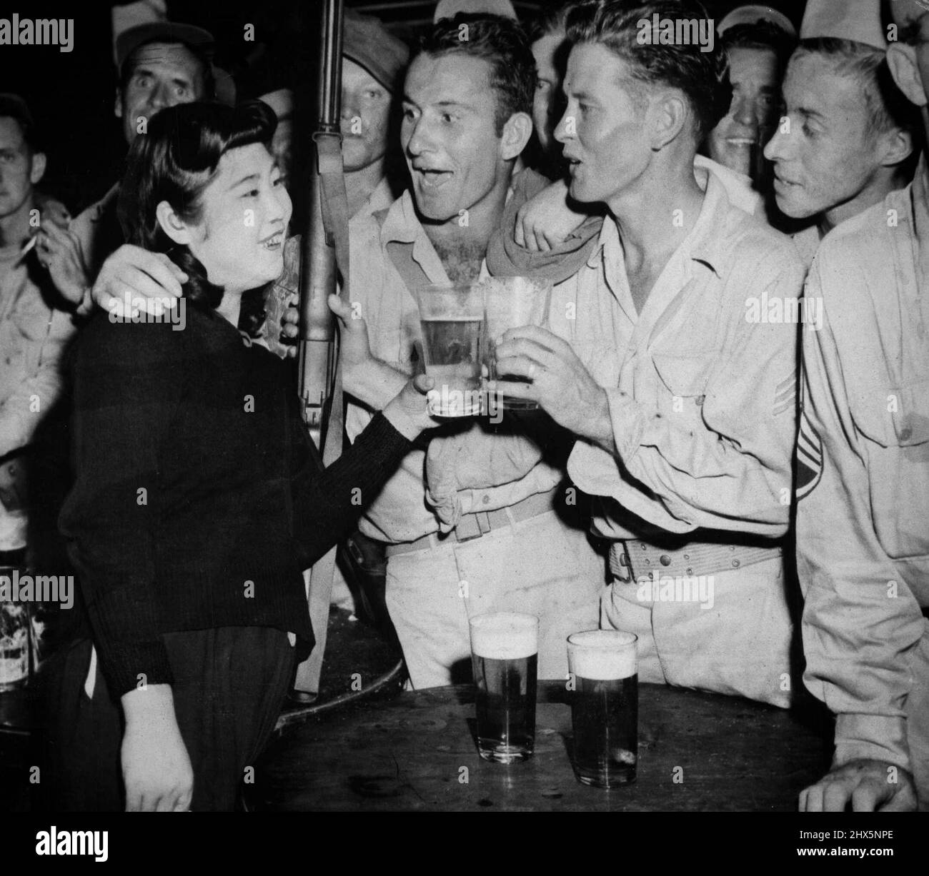 Bier für Amerikaner in Tokio - Ein japanisches Mädchen reicht Ein Glas Bier an PFC. Roy Peek, (links) von Henagar, ALA., während SGT. John T. Bruce, (rechts) aus Longworth, Texas, hält ein Glas im Club, der von der Freizeitvereinigung Recreation Amusement Association in Tokio eröffnet wurde. Der Club, der im Stadtteil Ginza eröffnet wurde, ist täglich von 3 bis 5 Uhr für die amerikanischen Besatzungstruppen geöffnet. Andere im Bild sind nicht ***** . 29. Oktober 1945. (Foto von Associated Press Photo). Stockfoto