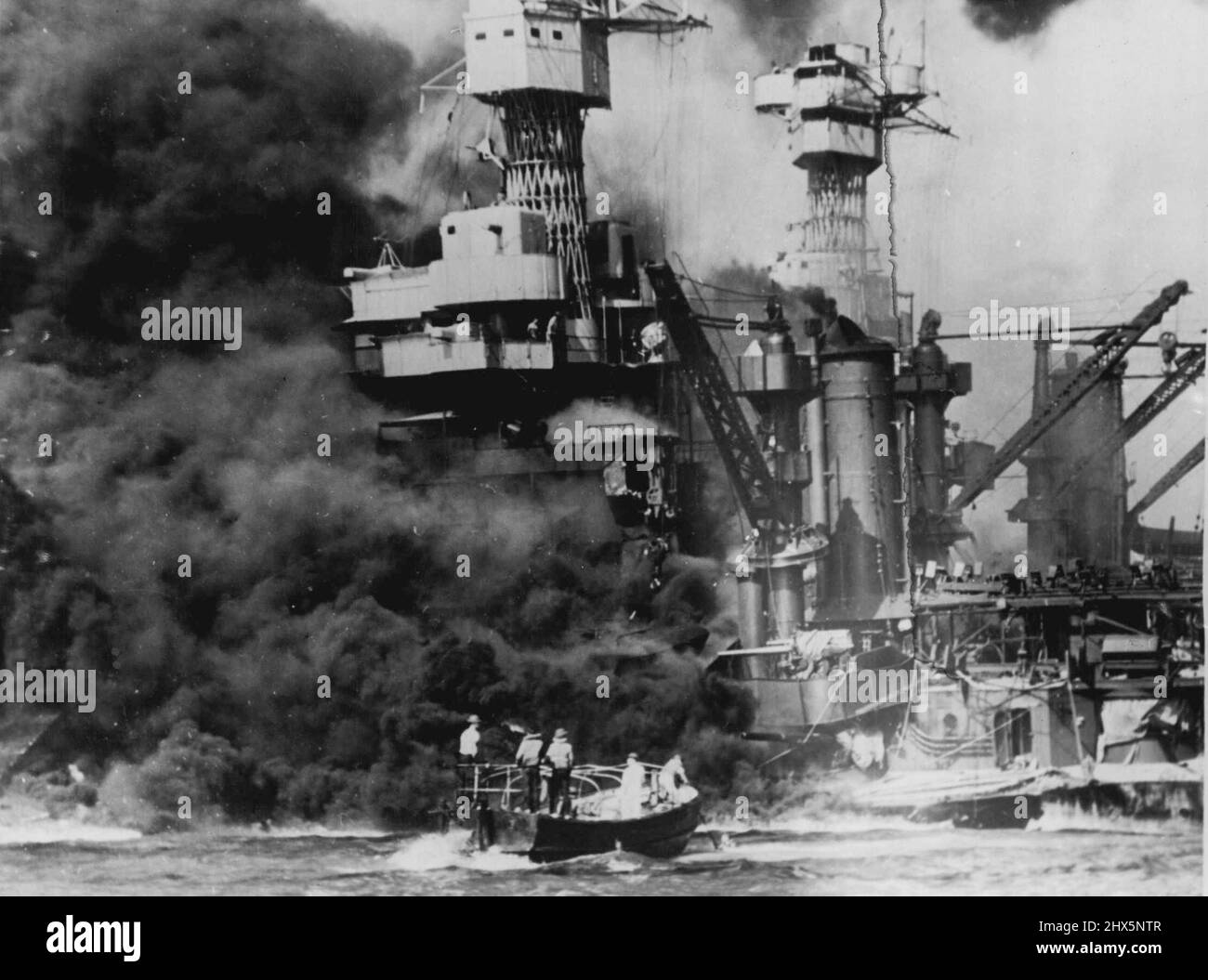 Ein kleines Boot rettet Seeleute aus den 31.800 Tonnen U.S.S. West Virginia brennt im Vordergrund. Rauch, der mittschiffs ausrollt, zeigt, wo der größte Schaden entstanden ist. Man beachte die beiden Männer im Überbau. Der US-Bundesstaat Tennessee ist im Boot. 26. Januar 1943. (Foto von Fox Photos). Stockfoto