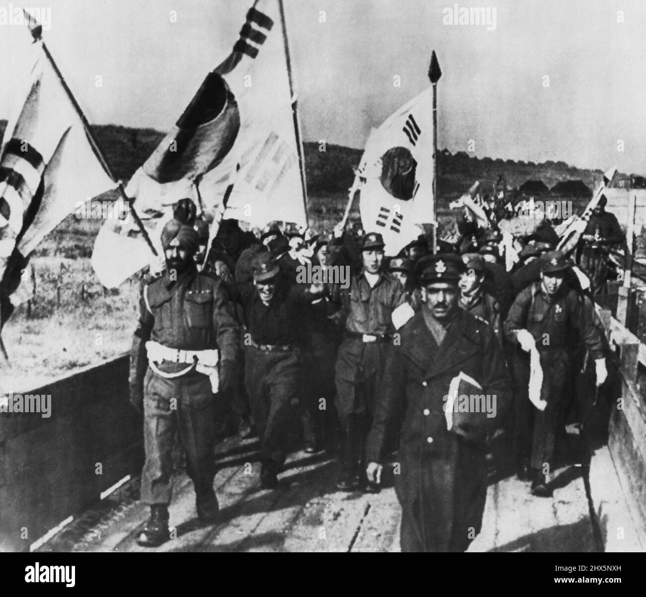 POWs an UN zurückgegeben -- Mit südkoreanischen Flaggen, Kriegsgefangenen, die von UN-Truppen in Korea gefangen genommen wurden und die keine Rückführung wollten, überqueren Sie die entmilitarisierte Zone in Panmunjom in eine Empfangsstelle, um von dem indischen Kommando, von dem zwei Mitglieder die Gruppe führen, in UN-Haft genommen zu werden. Von hier aus werden die Männer in Verarbeitungszentren gebracht. 20. Januar 1954. (Foto von AP Wirephoto). Stockfoto