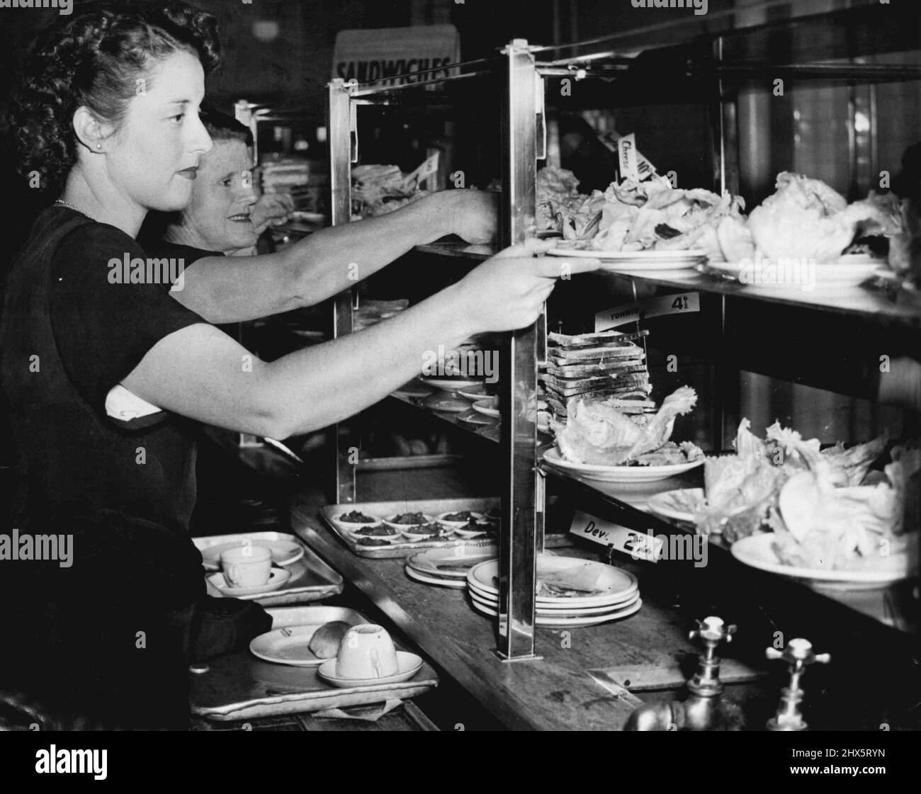 Mittagspause und unsere Verkäuferin nimmt gerne eine kurze Pause ein, entspannt ihre Schuhe ein wenig, während sie sich zum Essen hinsetzt. 22. Dezember 1949. Stockfoto