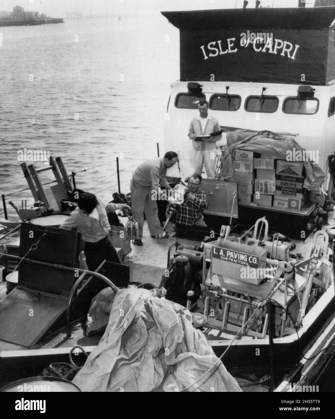 Um den Piratenschatz zu suchen -- an Bord der 110 Meter langen Insel Capri, einem umgebauten Marine-Tauchboot, werden mehrere Besatzungsmitglieder Vorräte verladen, die am Samstag vom Hafen von Los Angeles zur winzigen unbewohnten Cocos-Insel segeln werden, um $60.000.000 Piratenschatz zu suchen, von dem sie glauben, dass er dort begraben ist. John R. Beck übergibt Duane Wood einen Außenbordmotor, während Charles Williams, Organisator der Expedition, den Motor abprüft. Auf der linken Seite ist Tony Libordi. Williams glaubt, dass der Schatz aus Beute aus einer Kathedrale i besteht Stockfoto