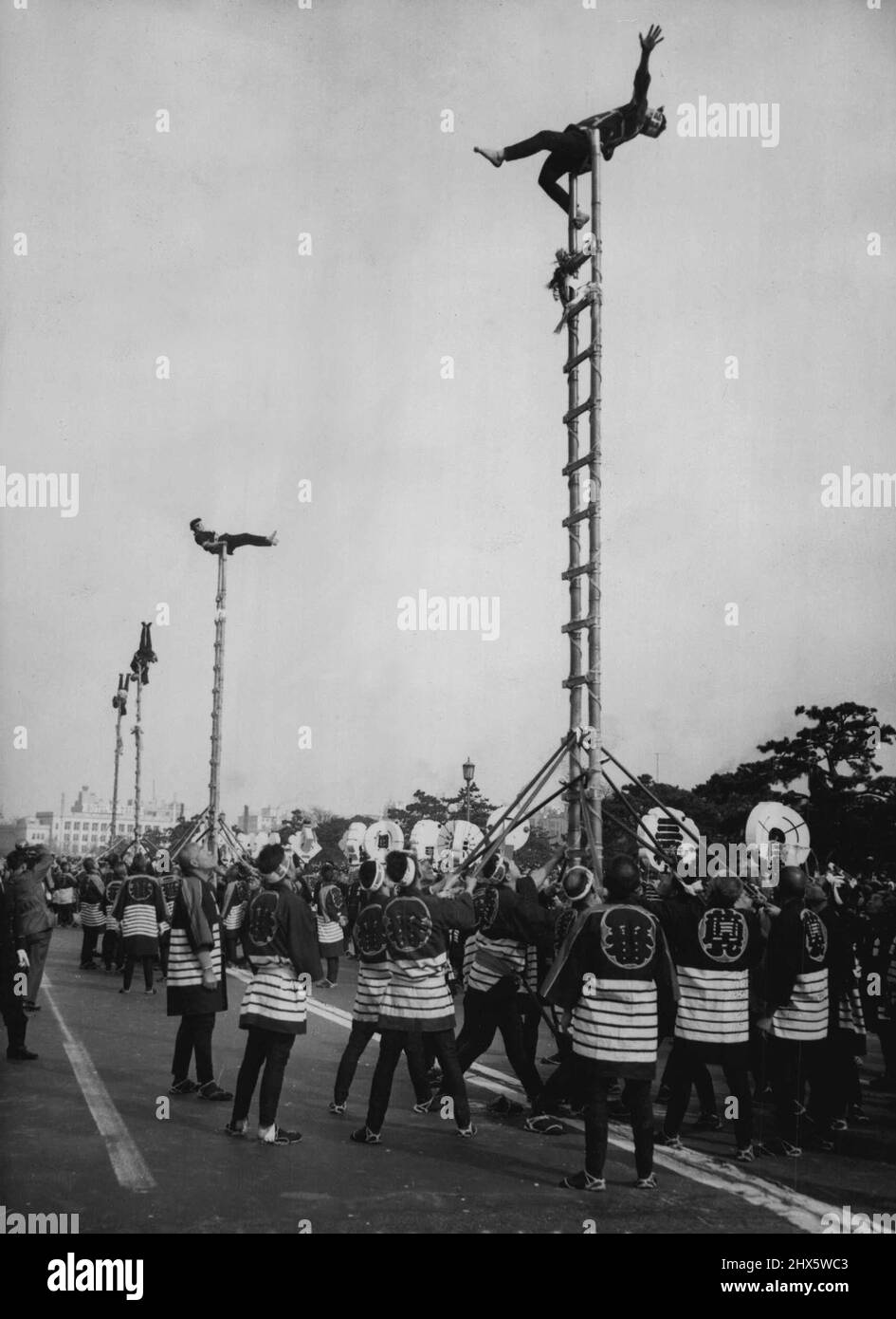 Japanische Feuerwehrleute veranstalteten kürzlich ihre farbenfrohe jährliche Parade auf dem Gelände des Kaiserpalastes in Tokio. Etwa 2.500 Feuerwehrmänner und 104 Motoren nahmen daran Teil. Dieses Bild zeigt Feuerwehrmänner, bekleidet mit traditionellen Happi-Mänteln, balanciert auf Bambusleitern, während ihre Kameraden akrobatische Ausstellungen zeigen. 21. Januar 1955. (Foto von Associated Press Ltd.). Stockfoto