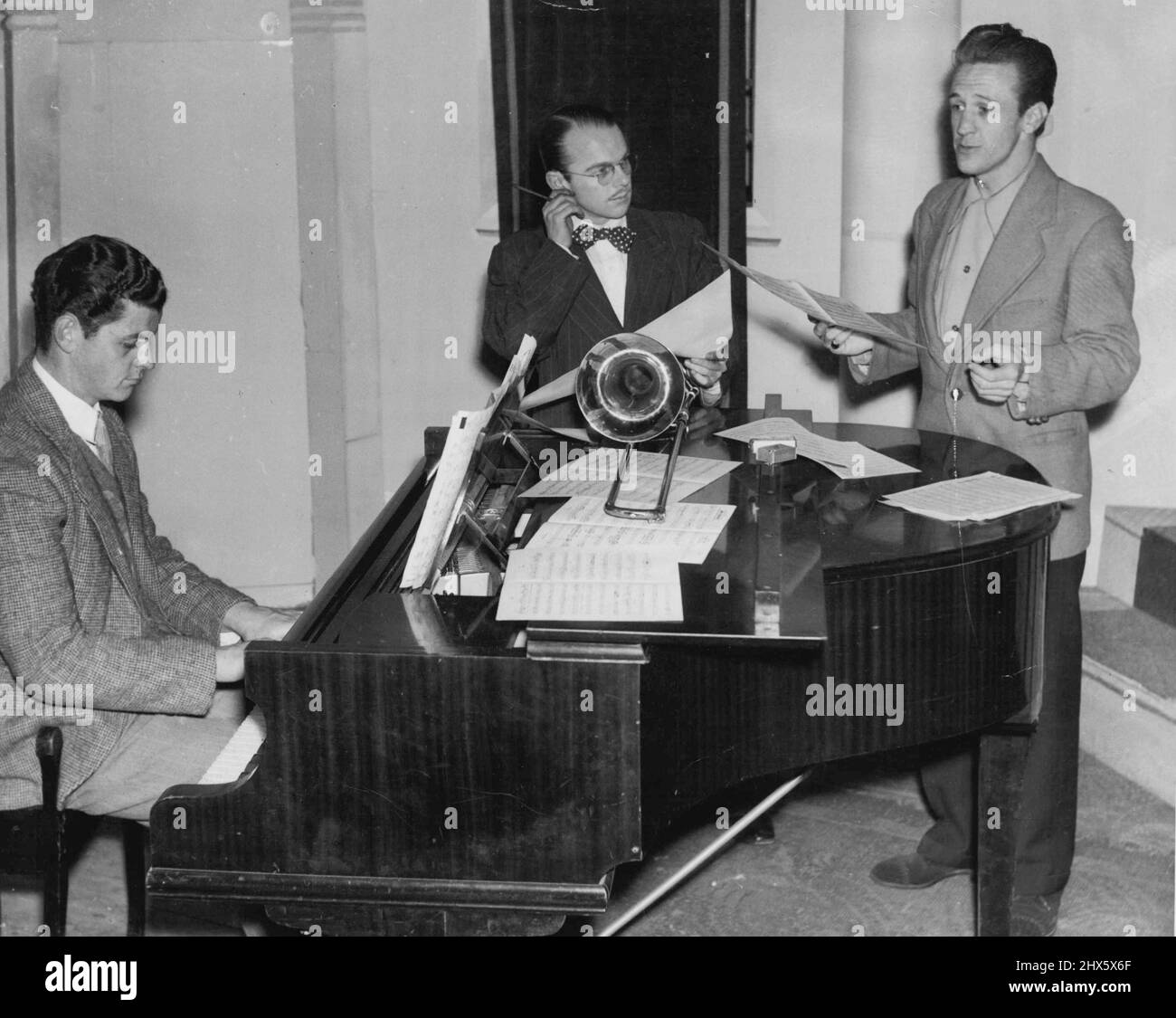 Billy Weston sieht nachdenklich aus und zieht ein Ohr, während er Norman Pearson eine neue Nummer singen hört. William Cathcart, ein Student des Konservatoriums, hilft am Klavier. Er hasst Jazz, liebt natürlich Klassiker. 21. Juli 1949. (Foto von Glamour). Stockfoto