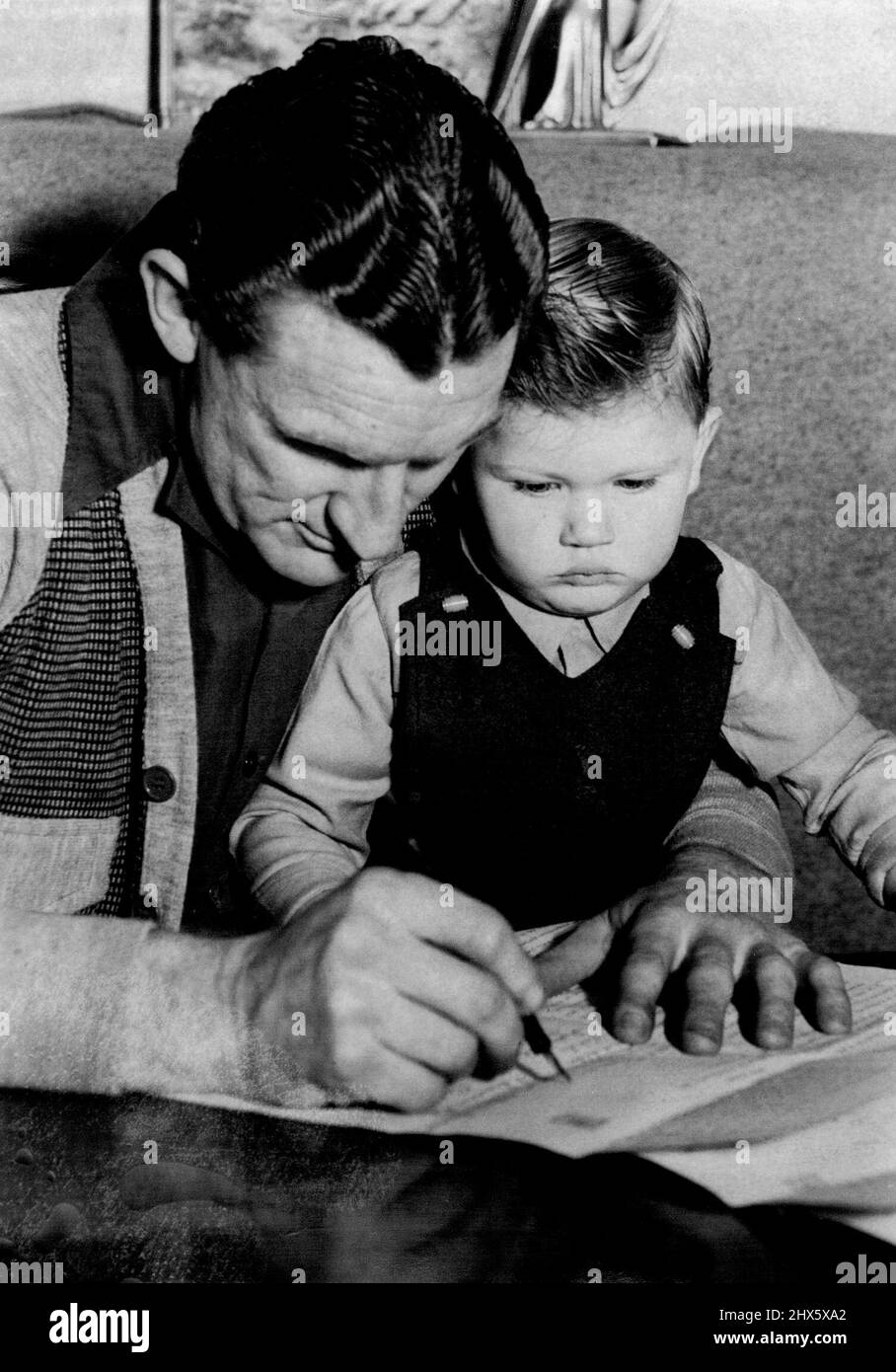 Cricketer W. Alley unterzeichnet den Colne Club-Vertrag, während sein 2½yr-alter Ken aufschaut. 6. August 1947. (Foto von Frank Albert Charles Burke/Fairfax Media). Stockfoto