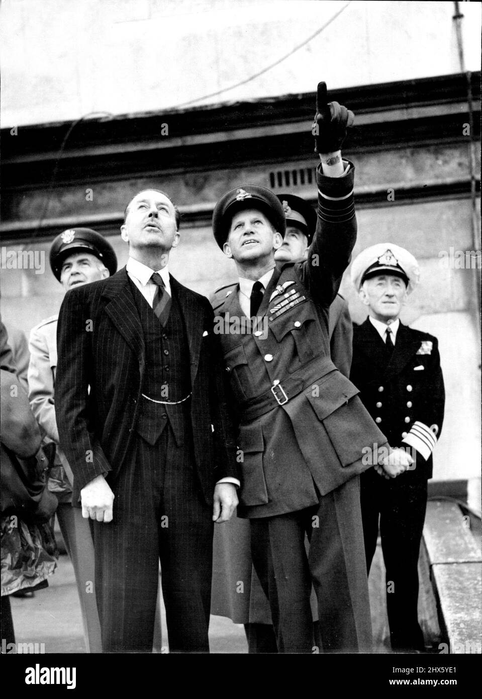 Fly-Past-Zeiger Für Alexander -- Air Chief Marshal Sir John W. Baker, stellvertretender Leiter des Air Staff, lenkte die Aufmerksamkeit von Lord Alexander (links), dem Verteidigungsminister, als sie heute (Montag) die Battle of Britain vom Dach der neuen öffentlichen Ämter in der King Charles Street, London, S.W. vorbeifliegen sahen. Über die Schulter des Air Chief Marshal Baker guckt der Feldmarschall Sir William Slim, der Chef des kaiserlichen Generalstabs, während auf der rechten Seite (hinten) Admiral Sir Rhoderick R. McGrigor steht. Erstens Stockfoto