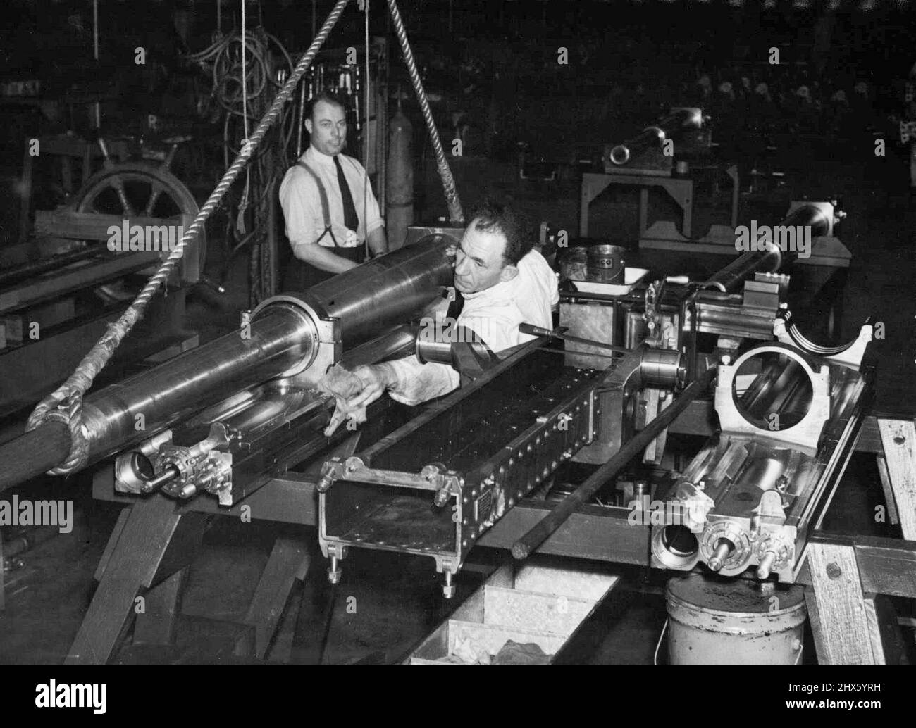 Ein Munitionsarbeiter legt den letzten Schliff an das glänzende Stahlfass eines 25-Pfünder-Feldkanonen in einer großen Fabrik in Sydney, wo die Montagearbeiten so schnell durchlaufen werden, wie die 4.000 Teile zur Hand kommen. Die Produktion dieser Waffen ist ein Triumph für das australische Unternehmen, erfordert Genauigkeit auf i/l0,00000.. Teil eines Zolls. 24. März 1942; Ein Munitionsarbeiter bringt den letzten Schliff an das glänzende Stahlfass eines 25-Pfünder-Feldkanonen in einer großen Fabrik in Sydney, wo die Montagearbeiten sind Stockfoto
