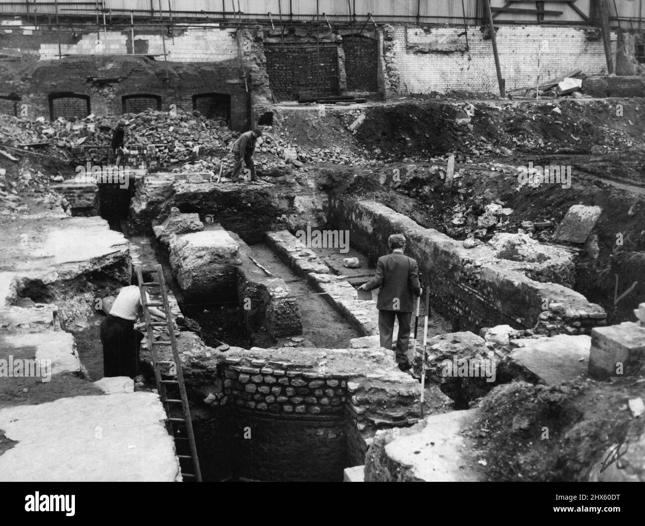 1600 Jahre Begraben. Arbeiter dachte, es sei Ein Stein. -- Herr F.W. Grimes (rechts) zeigt einem Kollegen auf der Website den Kopf von Mithras. Beim Graben auf der Stelle eines alten römischen Tempels in der Nähe des Herrenhauses hat gestern der Arbeiter Sam Thomas das ausgegraben, was er für einen Stein hielt. Ein Archäologe dachte anders und der Stein wurde als der Marmorkopf des heidnischen gottes Mithras identifiziert. Der Kopf, fein geschnitzt, trägt eine phrygische Mütze, Symbol des mithraischen Kults, und wurde am Bas begraben gefunden Stockfoto