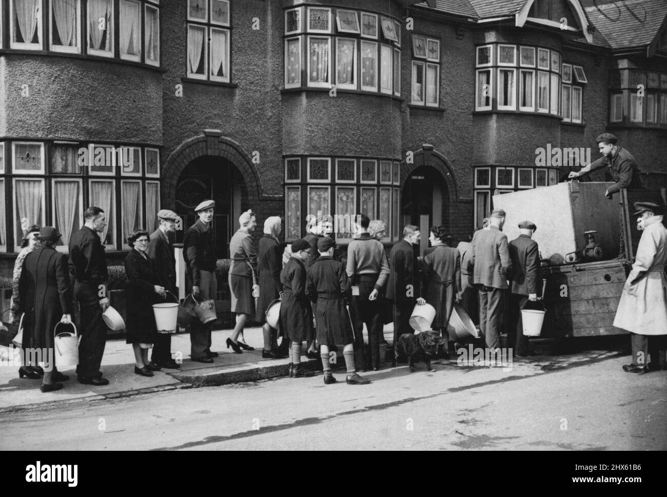 Truppen zur Hilfe überschwemmten Londons -- die lange Schlange, die jede Art von Utensilien trägt, wartet auf sie, während der Wasserwagen der Armee ihre dringend benötigte Versorgung bringt. Ein Bild aus Clapton, London. Soldaten, die viele Hunderte von mobilen Wassertankern mit sich brachten, wurden nun in den überfluteten Londoner Stadtteilen eingesetzt, wo große Gebiete aufgrund der steigenden Überschwemmungsgewässer, die die Stauseen und Werke überschwemmen, völlig ohne Hauswasserversorgung sind. 17. März 1947. ;Truppen Zur Hilfe Von Stockfoto
