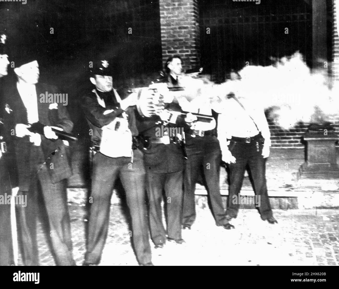 Gasgranaten in Akron Strike Riot feuern -- die Offiziere zeigten, wie sie Tränen- und Übelkeit-Gasgranaten in die wütige Schar von Streikenden und Sympathisanten schossen, die gegen die Tore des streikzerrissenen goodyear-Reifen- und Gummikol-Pflanzenbaums schossen. Man beachte das maschinenähnliche Aussehen der Gaswaffe, die von einem zweiten Offizier von links gehalten wird. 27.Mai 1938. (Foto von ACME).;Abfeuern von Gasgranaten in Akron Strike Riot -- Aufstellung der Offiziere zeigte Abfeuern von Träne und Übelkeit Gasgranaten in die aufrührerische Schar von Streikenden und Stockfoto