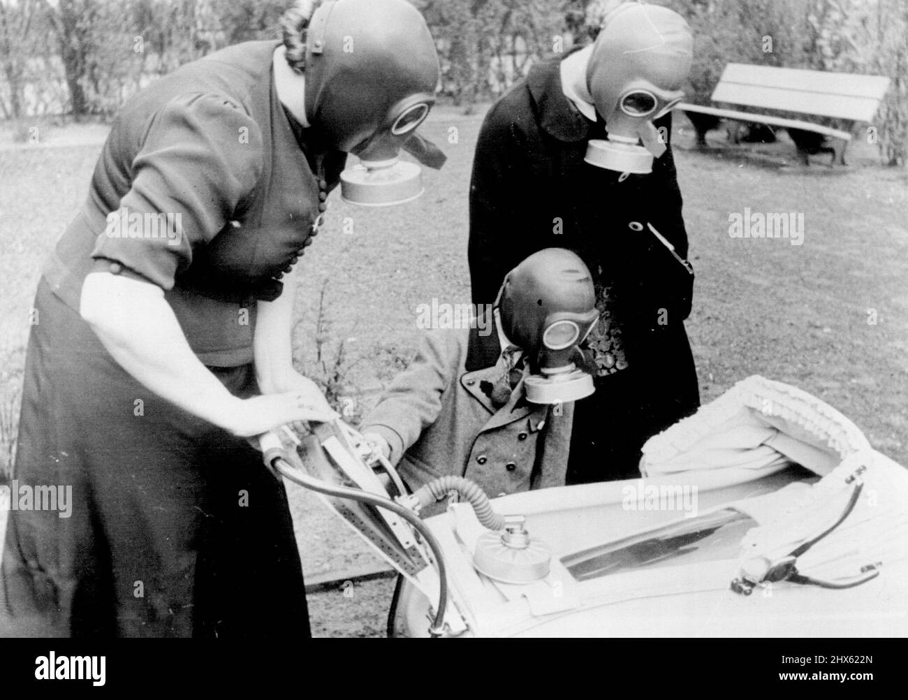 Deutsche Familien Sind Jetzt Alle 'Gasdicht'! -- Ein Baby in seiner gasdichten Wiege, nachdem er in seinen Kinderwagen gelegt worden war, mit seiner Mutter, Operation der Balgenluftpumpe auf den Kinderwagengriffen, kleiner Bruder und Tante, alle mit Gasmasken, schauend an. Wie in Frankreich und Großbritannien wurden nun Gasmasken an alle deutschen Familien ausgegeben. Die Designs der Masken sind von unterschiedlichen Typen, geeignet für Erwachsene, Kinder und Babys, wobei der letzte Name in einer Art gasdichte Wiege gelegt wird, die von einem b betrieben wird Stockfoto