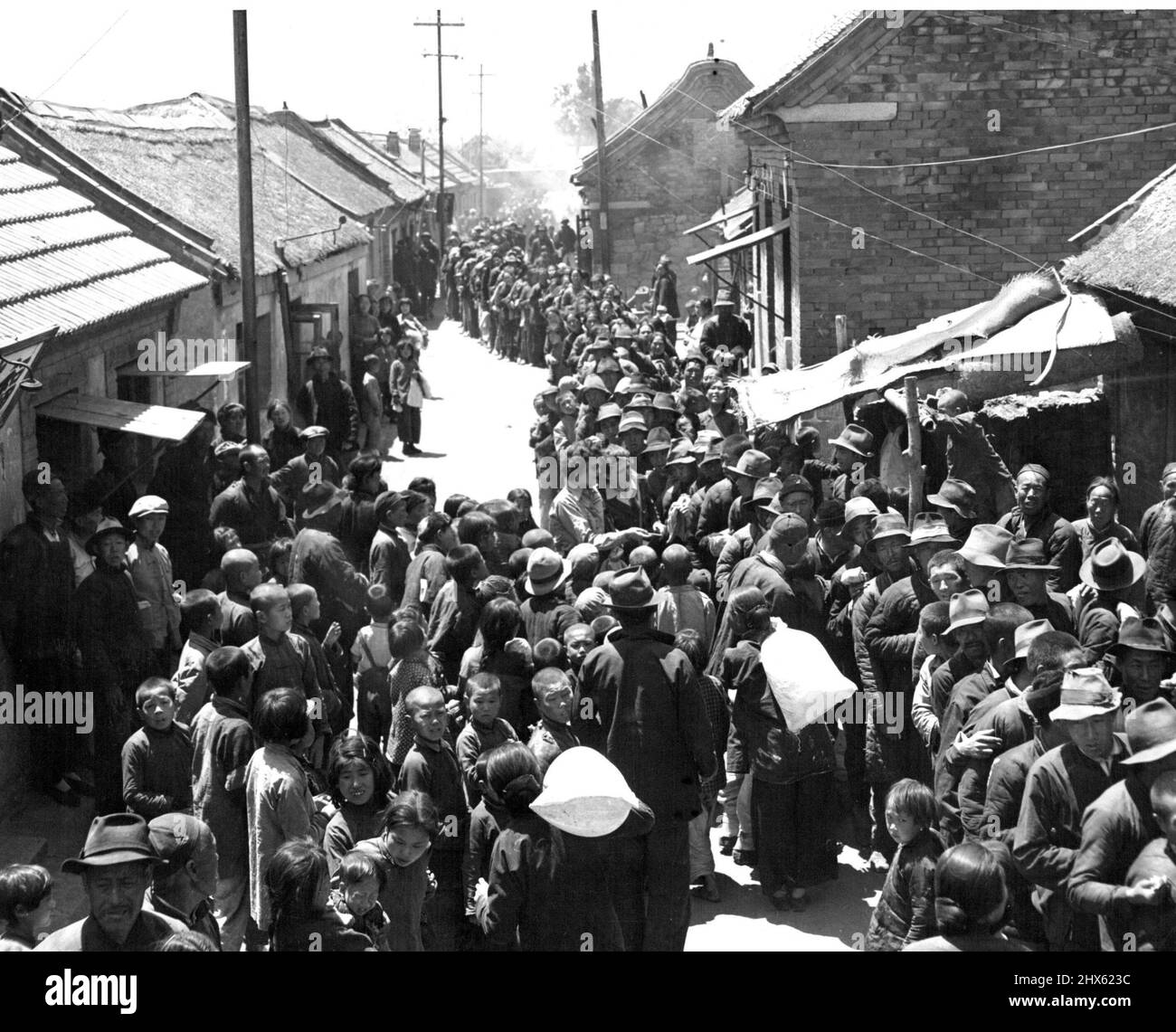 Village Relief -- die gesamte Bevölkerung des Dorfes Li Chuan -- 12 Meilen von Tsingtao -- Reihen sich an, um UNRRA-Mehl zu erhalten, das von CNRRA verteilt wird. Fünf Pfund Mehl wurden an jeden dieser improverished Shantung Peninsula Dorfbewohner gegeben. Bei der Untersuchung eines der Mehlsäcke in der Mitte (von links nach rechts) sind Ann Cottrell aus Richmond, VA., UNRRA China-Korrespondentin, und Verna M. Feuerhelm von Hayward Calif. 24. Juni 1946. (Foto von Michael Arthur/Fairfax Media);Village Relief - Stockfoto