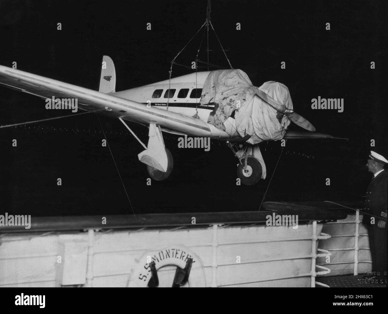 Schnellstes 'Flugzeug in Australien -- Entladen eines Lockheed Orion, der 220 m.p.h. vom Liner 'Monterey' in der letzten Nacht um Mitternacht erreichen kann. Diese Maschine, geflogen von Captain J.P. Dickson wird in Begleitung von Arthur M. Loew, First Vice President Metro-Goldwyn Mayer Picturs, und Rosthal am Samstag, Montag in Adelaide und Dienstag in Wyndham nach Melbourne fliegen und von dort den bisher größten kommerziellen Weltflug starten. Vacuum Oil Company hat Lieferungen arrangiert. Die Lichter der Hafenbrücke von Sydney sind zu sehen Stockfoto