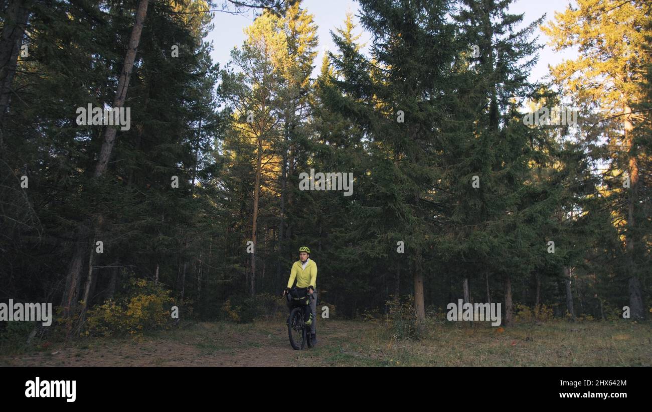 Der Mann reist auf gemischtem Terrain mit Bikepacking im Freien. Die Reise des Reisenden mit Fahrradtaschen. Stylische Bikepacking-, Bike-, Sportbekleidung in grün-schwarzen Farben. Magischer Waldpark. Stockfoto