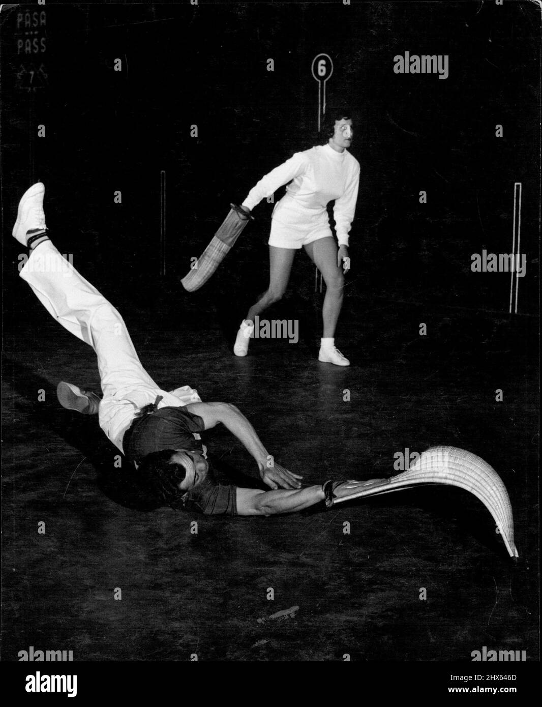 Girl 'Jai-Alai' Spieler (9): Du musst nicht nur Wände klettern, sondern auch manchmal auf dem Boden kraxeln, wenn du Jai-Alai spielst. Dieser Action-Schuss hat den Profispieler Tiburcio Celaya erwischt, der auf dem Boden abgetaucht ist, um einen Tiefschlag zu erhappen und eine Rückkehr zu machen. Alicia Weeks, im Hintergrund, wagt sich, Celayas Schuss zurückzugeben. 1. April 1954. (Foto von Ben & Sid Ross). Stockfoto