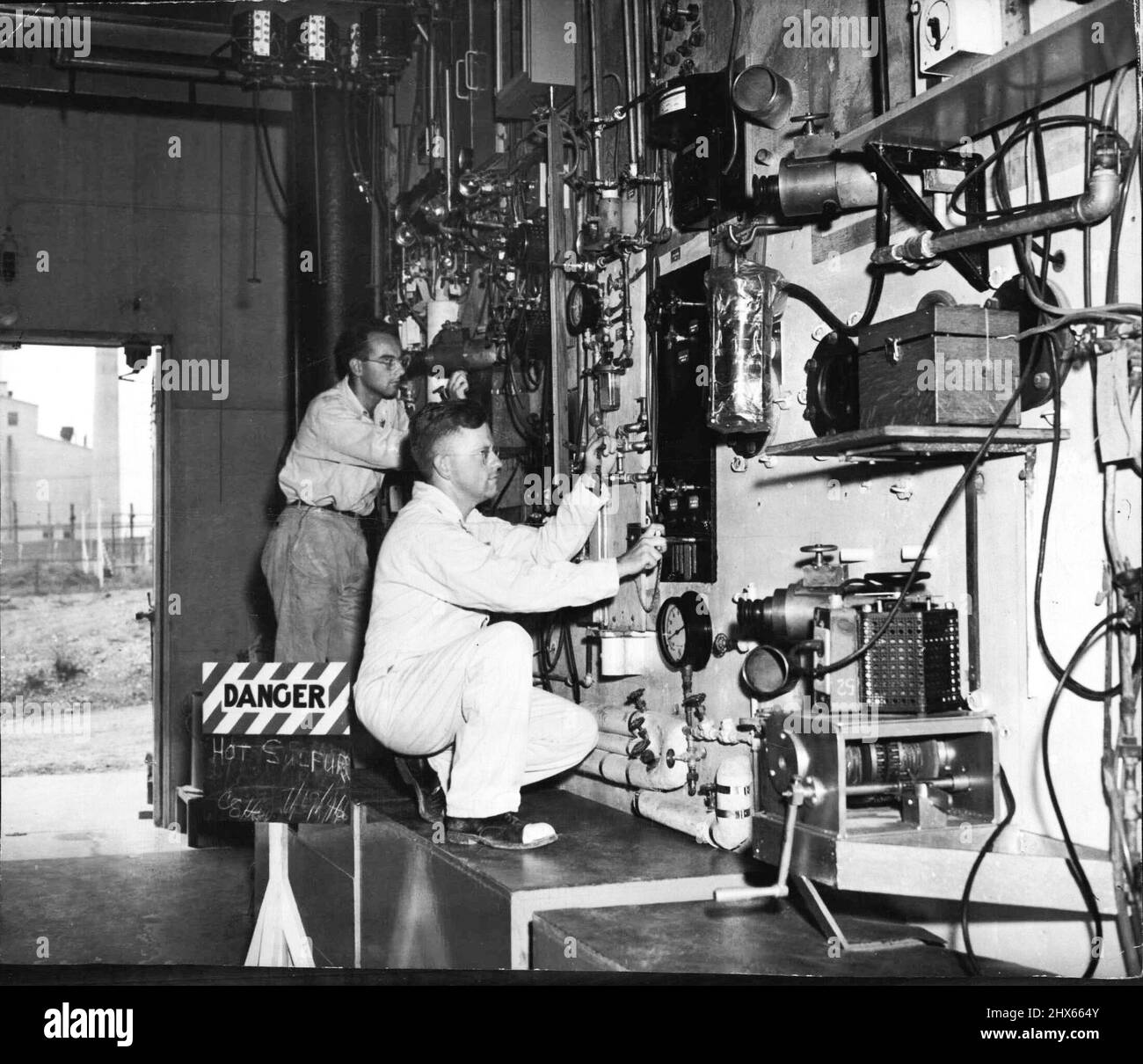 Operate Controls in Atom Plant Project -- an einer Fernbedienungstafel für ein 'heißes' Labor im Oak Ridge, Tennessee, Atomkraftwerk-Projekt, August 2, sind John H. Rauscher (links), Forscher-Solvent-Ingenieur, der durch abgeschirmtes Mikroskop schaut, und G. M. Herbert (rechts), Forscher-Chemiker, der die Bedienelemente justiert. Der Sing (links), „Wut“, weist auf Grund der Kontrolle, Board, was die Operation ermöglicht, die radioaktive Spezies in der Menge für die Produktion des Isotops extrahiert, um in medizinischen Resea verwendet werden Stockfoto