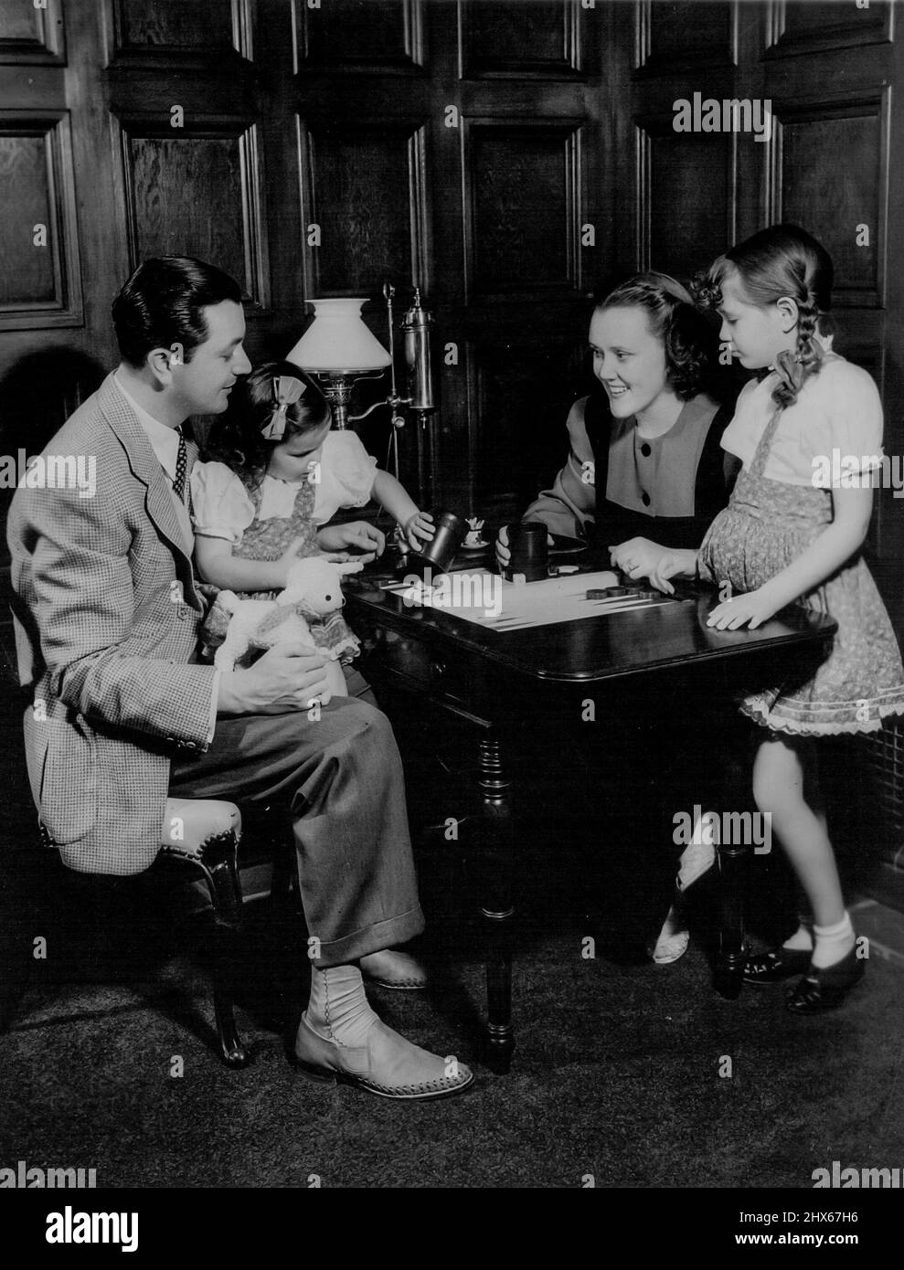 Robert Young - widmet seine Zeit, wenn nicht in Bildern zu arbeiten, seiner Familie und zu Hause in San Fernando Valley. Der Schauspieler, der jetzt in einem neuen Metro-Goldwyn-Mayer-Film mit Eleanor Powell und Ann Sothern auftritt, verfügt über ein 7 Hektar großes Anwesen, das zu den Showplaces Hollywoods zählt. Carole Ann-und Barbara Queen Young spielen zusammen mit Papa und Mama Backgammon. Fünf bzw. sieben Jahre alt, sind sie der Apfel des Auges ihres Vaters. 25. April 1942. Stockfoto