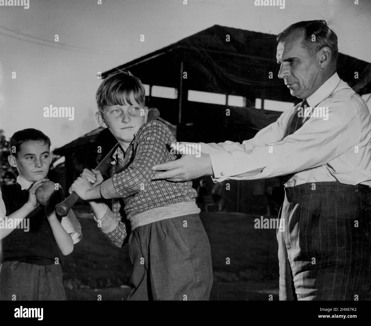 Gordon Young, NSW Director von National Fitness, demonstriert Softball. (L-R): Glen McKeller (11), Trevor Nikitin (11), beide von Willoughby Pub. Schule im Willoughby Park Child Care Scheme. 30. Juli 1951. Stockfoto