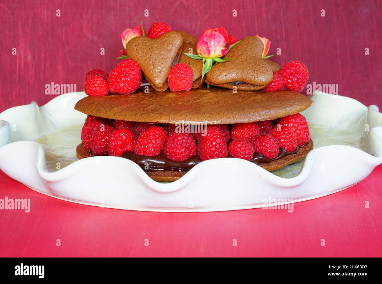 Ein riesiger Makkaronkuchen aus Schokolade mit frischen Himbeeren und Rosenblüten Stockfoto