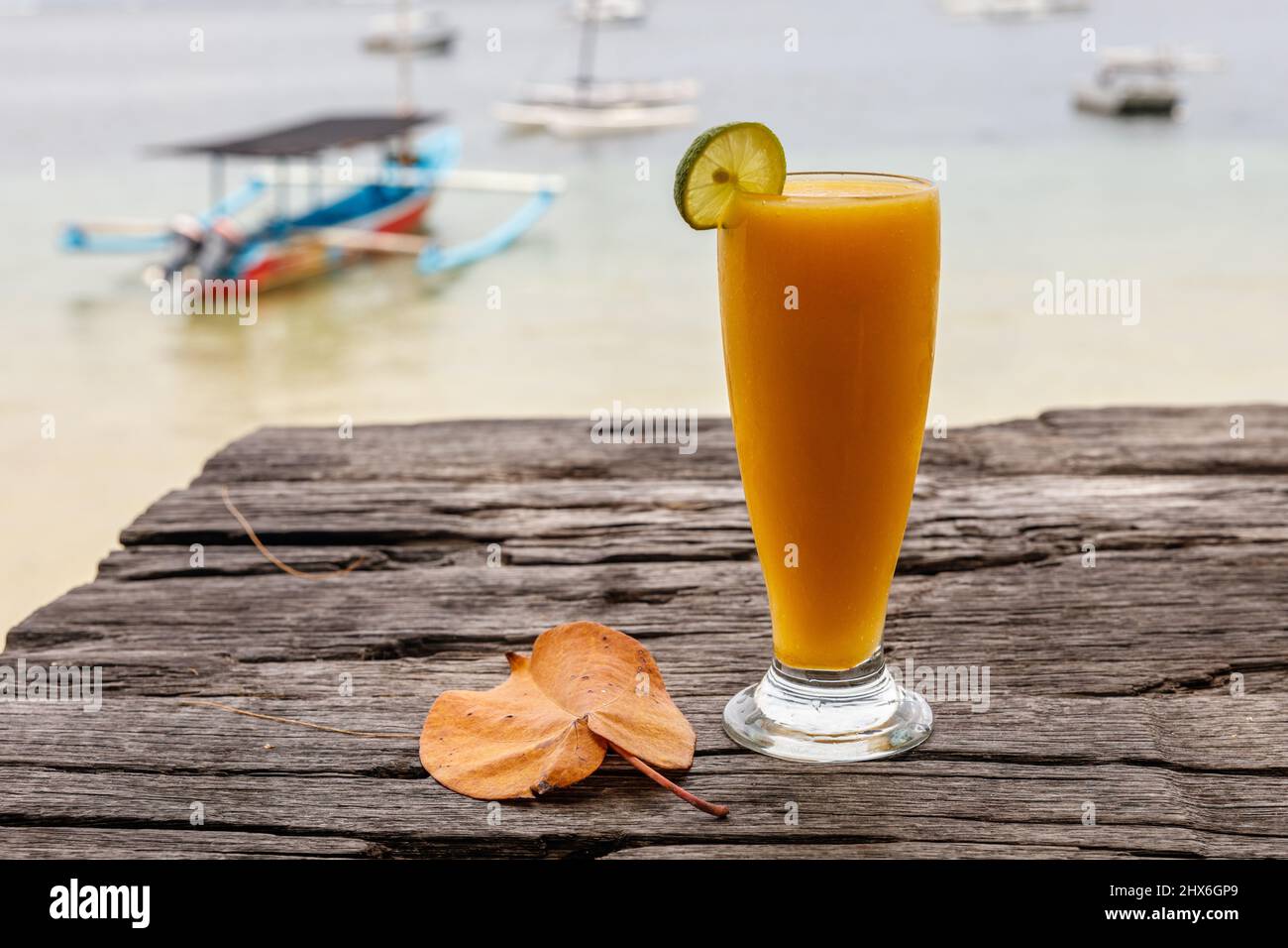 Mango-Saft am Strand mit dem Meer und einem Boot im Hintergrund. Sanur, Bali, Indonesien. Stockfoto
