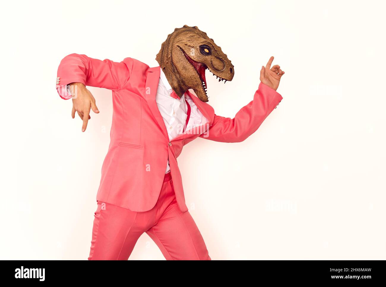 Lustiger Mann in einem pinken Anzug und einer Dinosaurier-Maske, der auf einer verrückten Party tanzt und Spaß hat Stockfoto