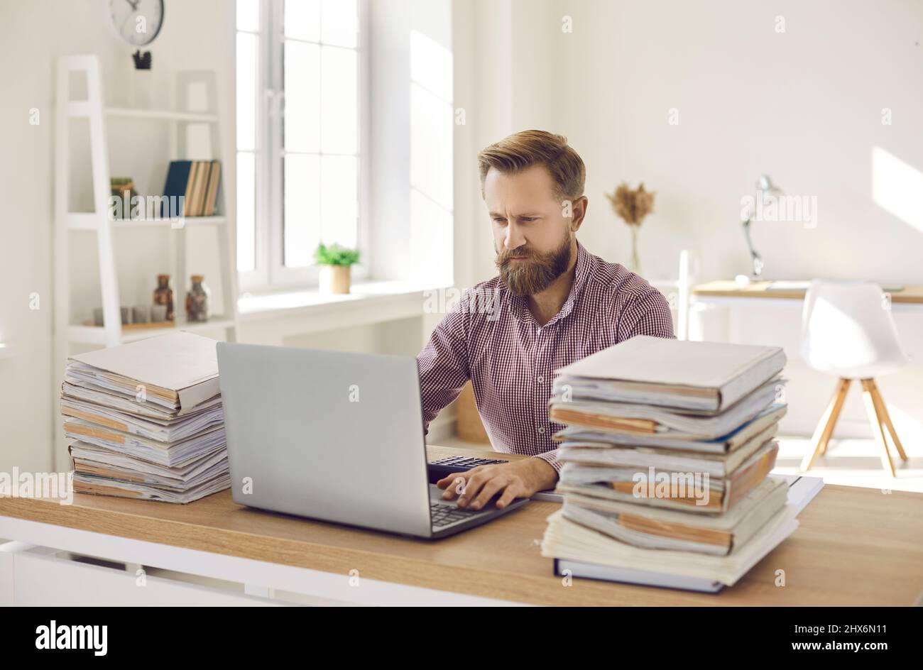 Seriöser Buchhalter, der mit Papierkram an seinem Schreibtisch sitzt und an seinem Laptop arbeitet Stockfoto