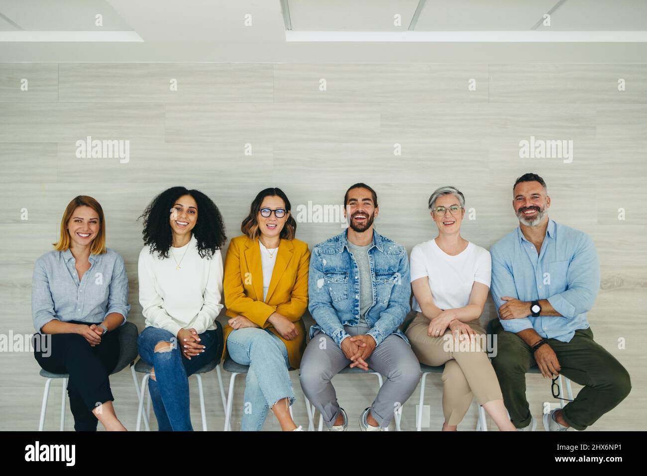 Erfolgreiche Bewerber lächeln an der Kamera, während sie in der Schlange für ein Interview sitzen. Gruppe multikultureller Geschäftsleute, die auf einen Opportuni warten Stockfoto