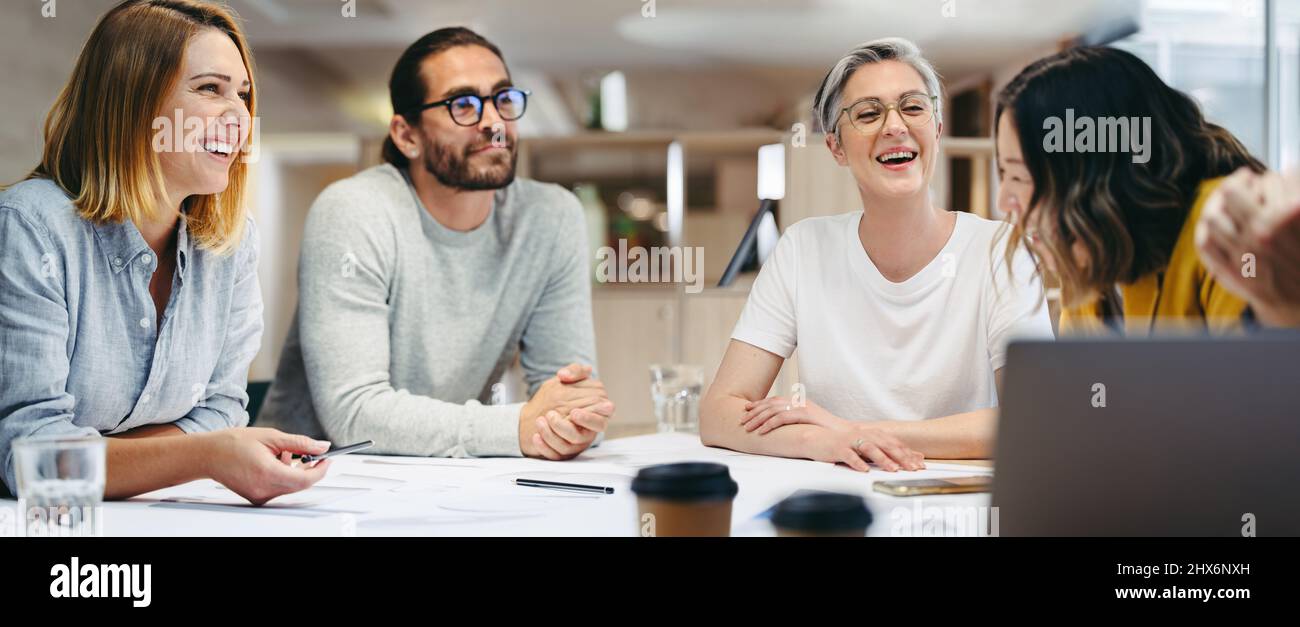 Fröhliche Design-Profis lächeln fröhlich während eines Meetings in einem modernen Büro. Gruppe innovativer Geschäftsleute, die während des Aufenthalts kreative Ideen austauschen Stockfoto