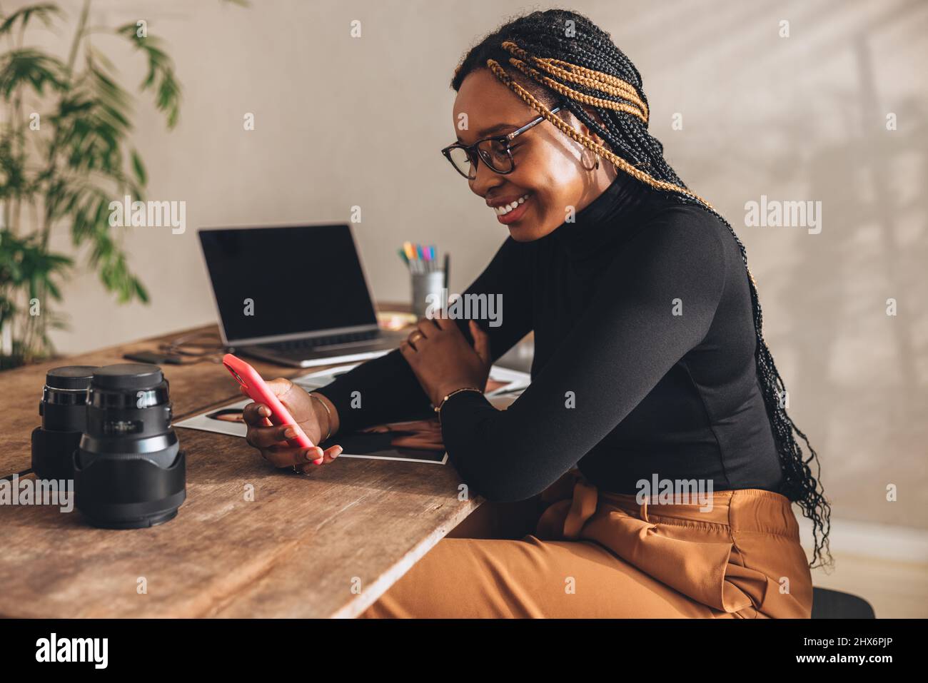 Kommunikation mit Kunden. Glückliche Fotografin lächelt fröhlich, während sie einen Videoanruf auf ihrem Smartphone anruft. Kreative junge Fotografin arbeitet Stockfoto