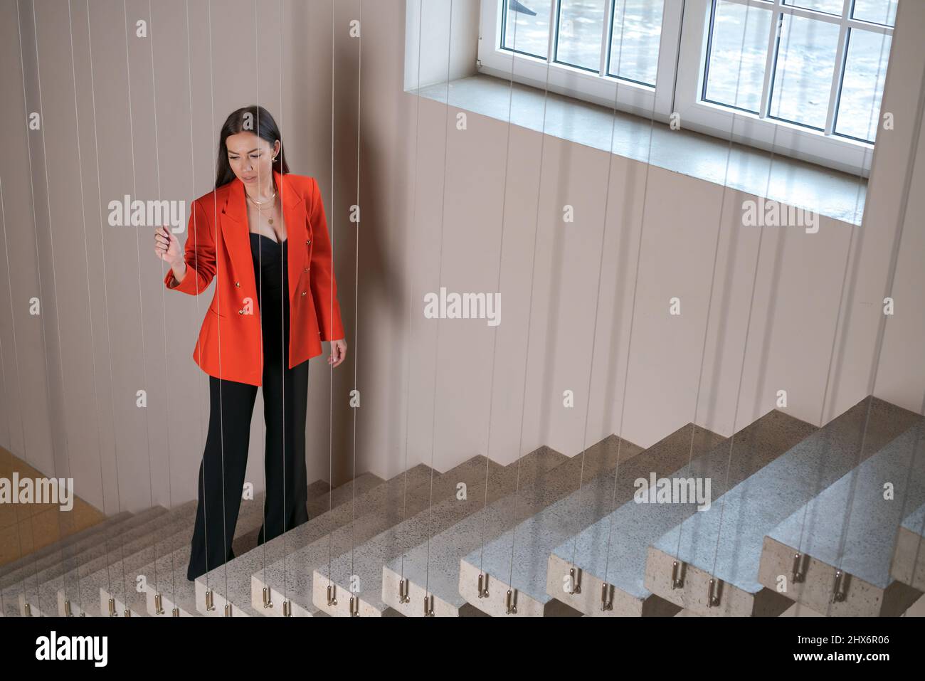 Geschäftsfrau in roter Jacke steht mit durchdachtem Blick auf Treppen, denkt über einen Businessplan für die Zukunft nach, sorgt sich um die zukünftige Finanzkrise Stockfoto