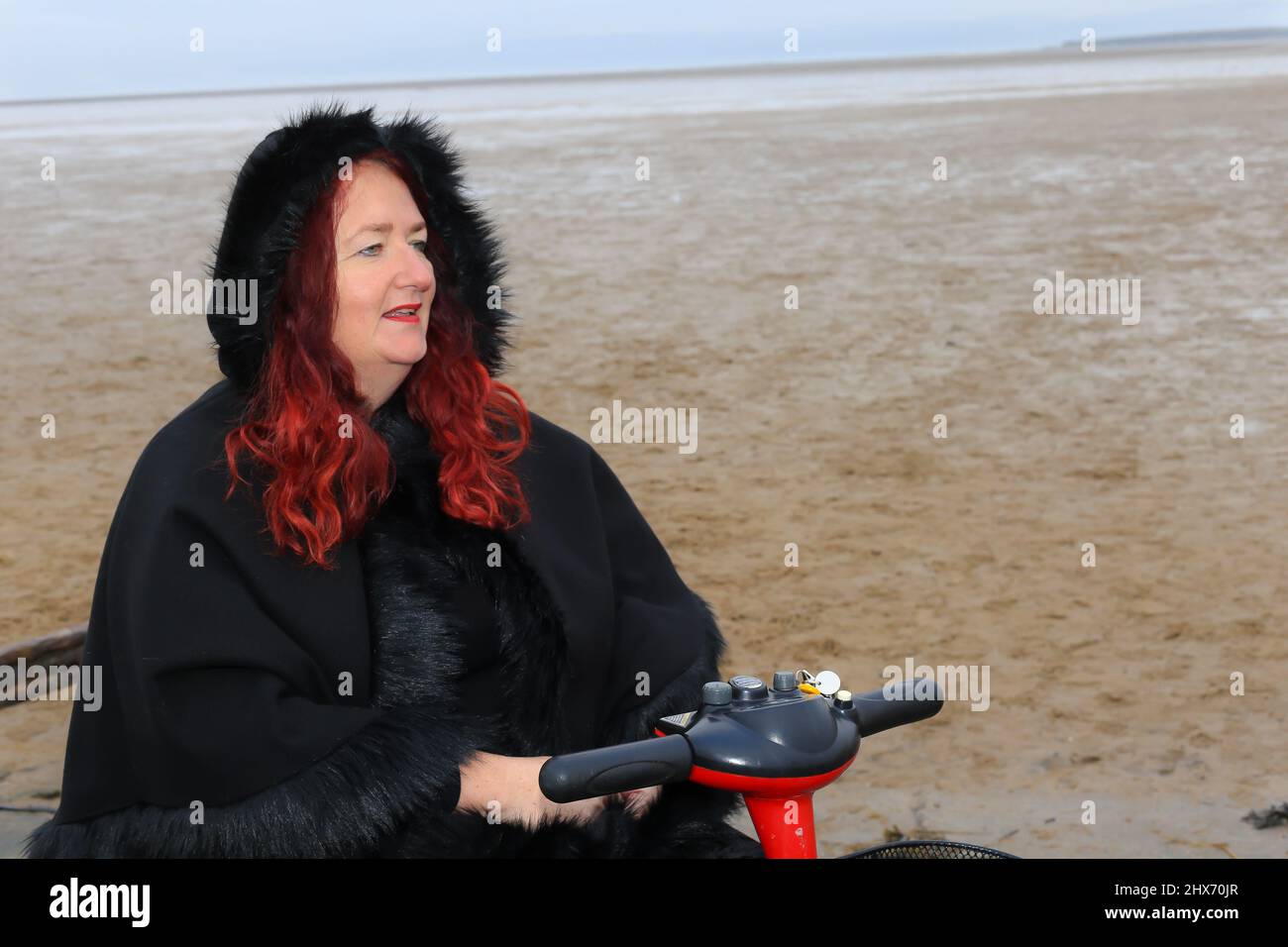 Frauen mit roten Haaren fahren am Strand mit einem Mobilitätsroller Stockfoto