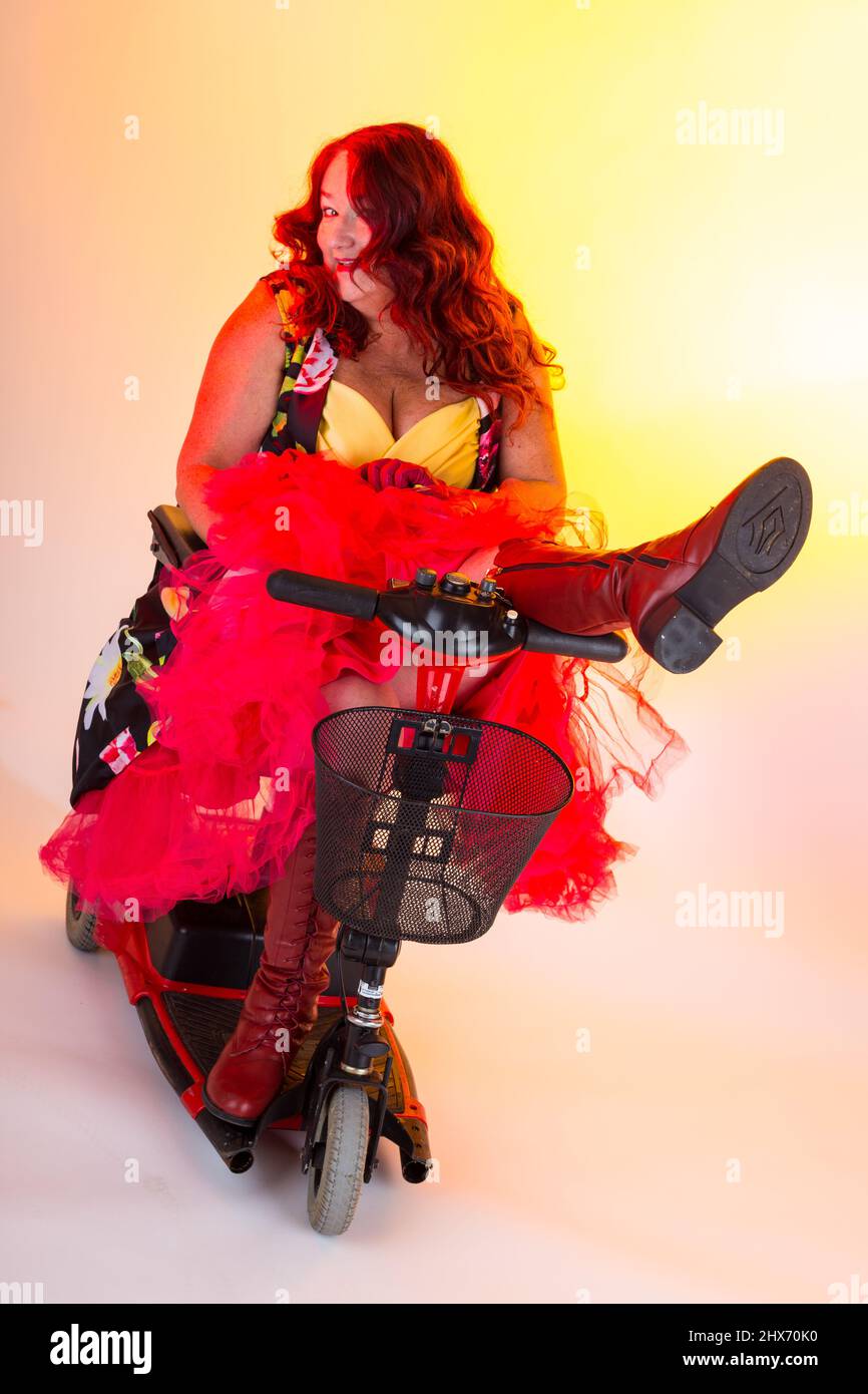 Lebhafte Frauen auf einem mobilen Roller, die für ein Fotoshooting in einem Studio posieren Stockfoto