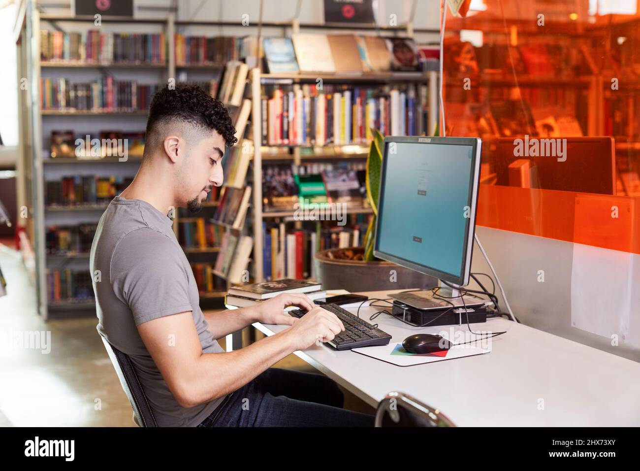 Männlicher Student, der Computer in der Bibliothek benutzt Stockfoto