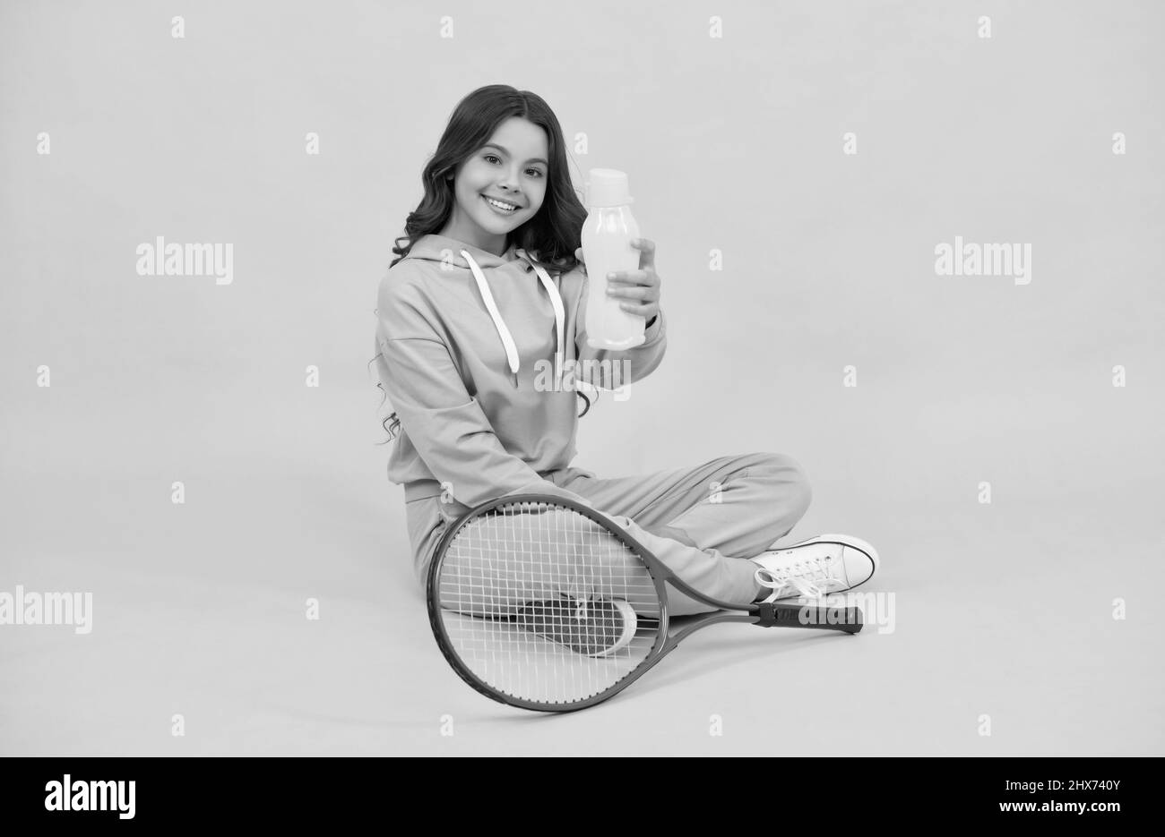 Kind sitzen mit Schläger und Wasserflasche. Kind mit Tennisschläger. Teen Mädchen trinken Wasser Stockfoto