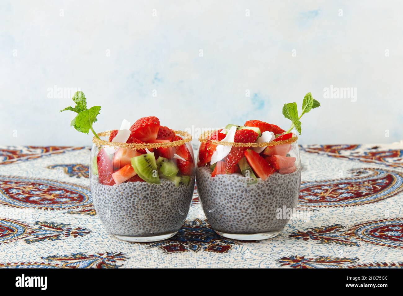Blick aus der unteren Ecke auf Chia Pudding Dessert mit Sommerbeeren, Erdbeeren, Kiwi und Kokosnussscheiben, verziert mit einem Minzzweig. Keine Personen. Stockfoto