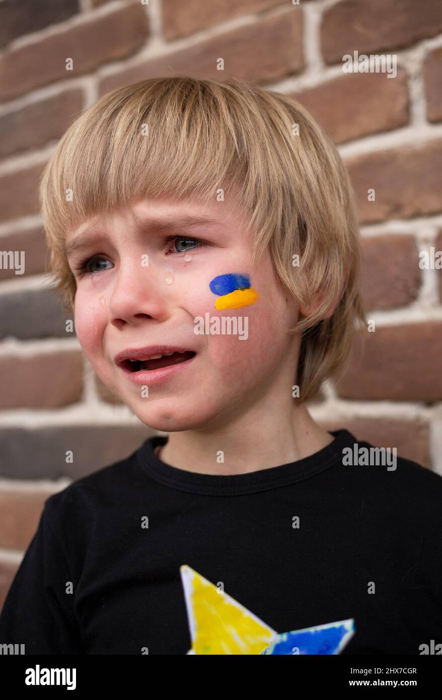 Gesicht eines weinenden, verängstigten Jungen, gelb-blaue ukrainische Flagge auf seine Wange gemalt. Russlands Invasion der Ukraine, Bitte um Hilfe für die Weltgemeinschaft. Stockfoto