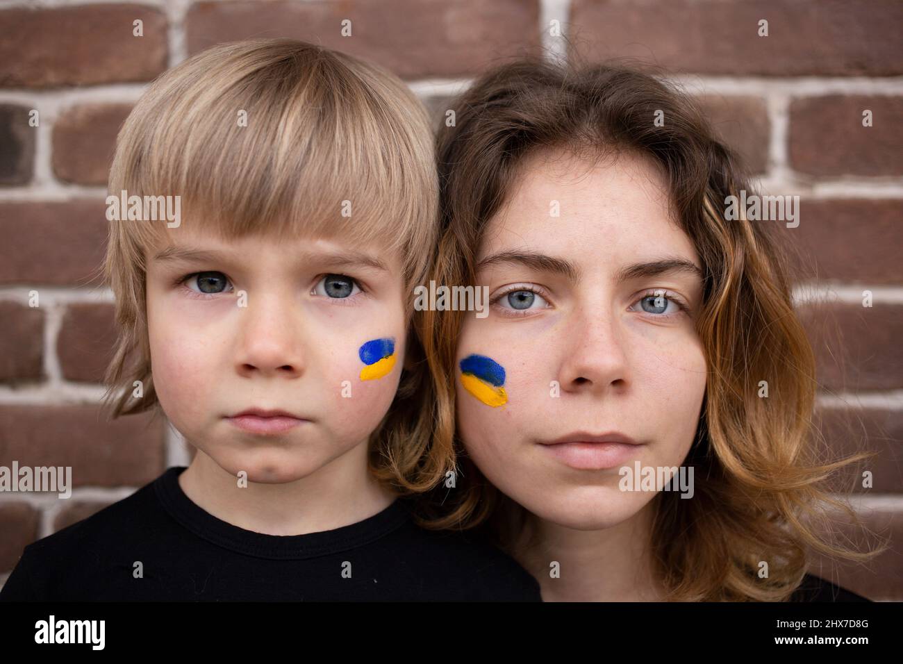 Gesichter von Jungen und jungen Frauen mit blauer und gelber Flagge auf Wangen. Familie, Einheit, Unterstützung. Ukrainer sind gegen den Krieg. Um Hilfe bitten Stockfoto