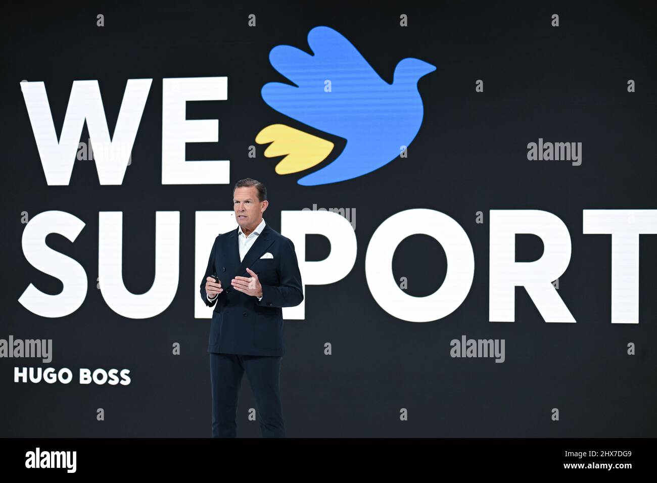Filderstadt Sielmingen, Deutschland. 10. März 2022. Daniel Grieder, CEO des Modekonzerns Hugo Boss, steht auf der Pressekonferenz zum Abschluss vor einem Videoleinwand mit der Aufschrift: 'Wir unterstützen' und einer Friedenstaube in den Farben der Ukraine. Quelle: Bernd Weißbrod/dpa/Alamy Live News Stockfoto